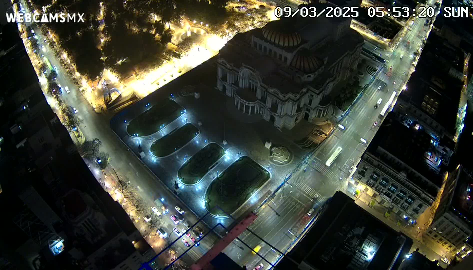 A nighttime, aerial view of a large building, possibly a museum, surrounded by streets, illuminated landscaping, and other buildings.