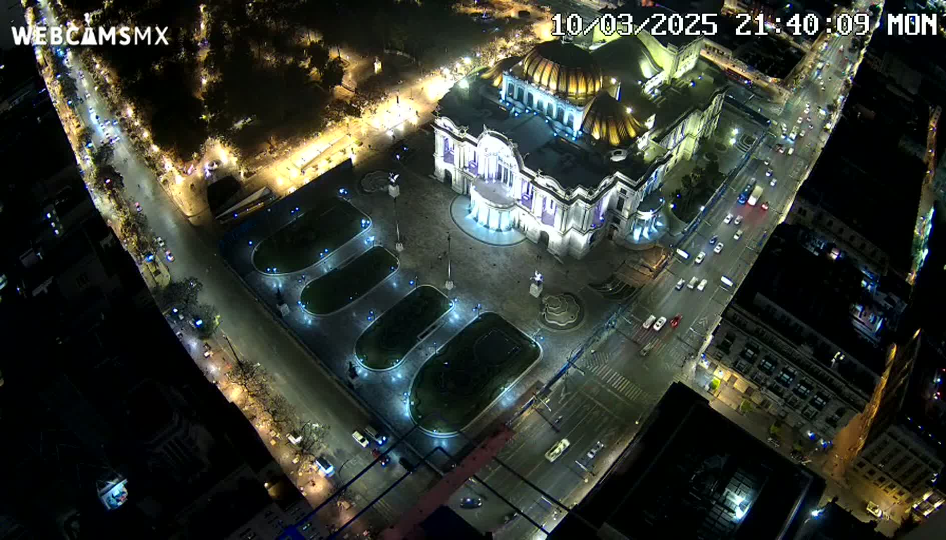 An illuminated Palacio de Bellas Artes at night is surrounded by city streets with cars and lights, under a dark sky.