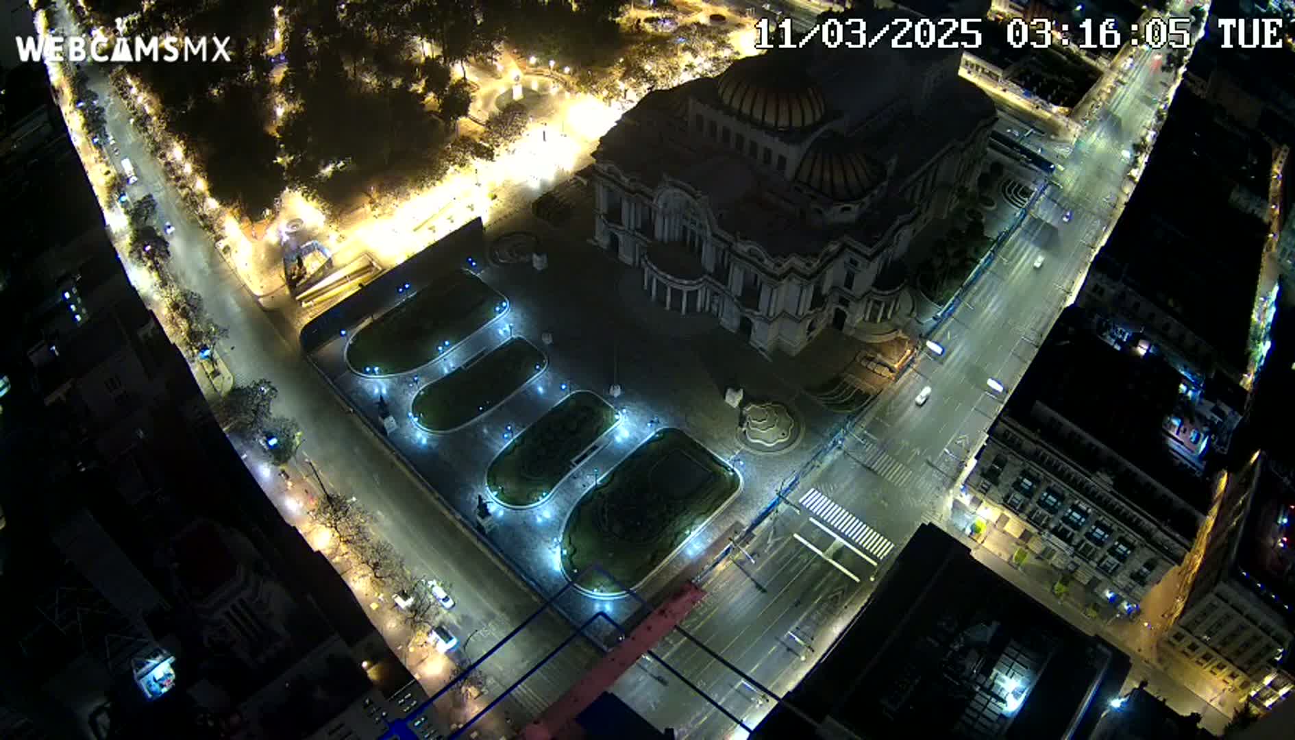 An aerial nighttime view shows a large building with a dome, surrounded by illuminated streets and a plaza with several oval-shaped gardens.