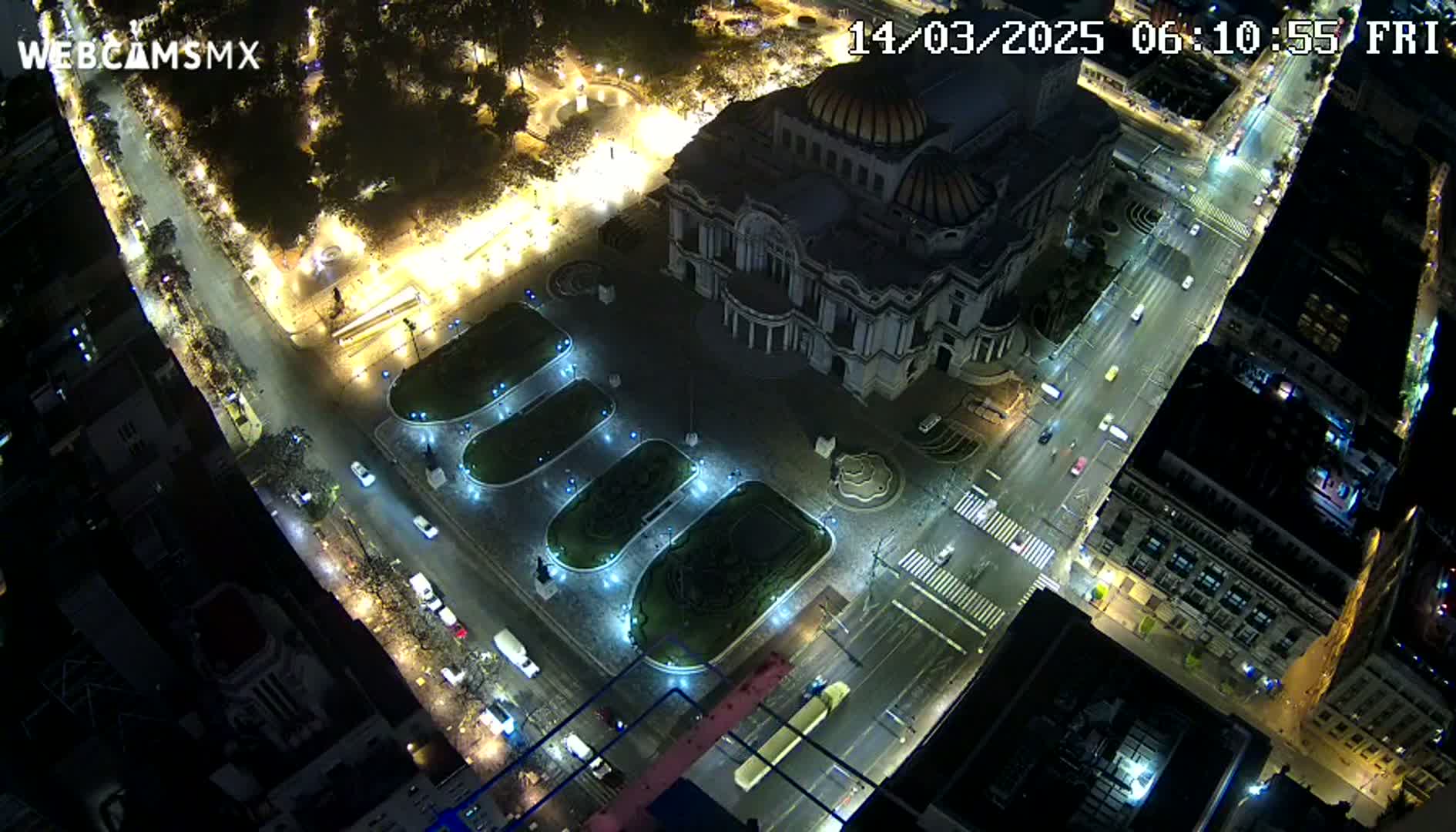 An aerial nighttime view shows a large building surrounded by a plaza with illuminated landscaping and streets with sparse traffic.