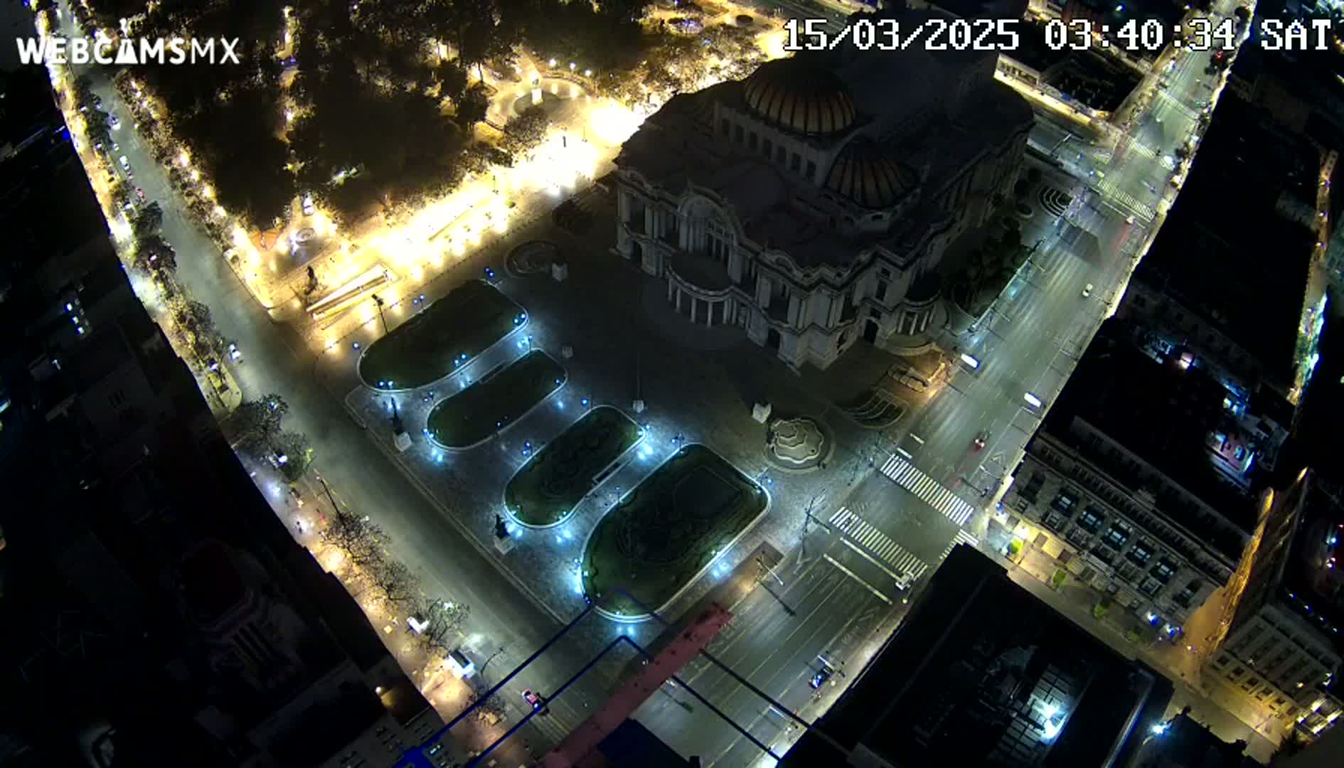 A nighttime aerial view of a large building, possibly a museum, surrounded by empty streets and illuminated gardens.