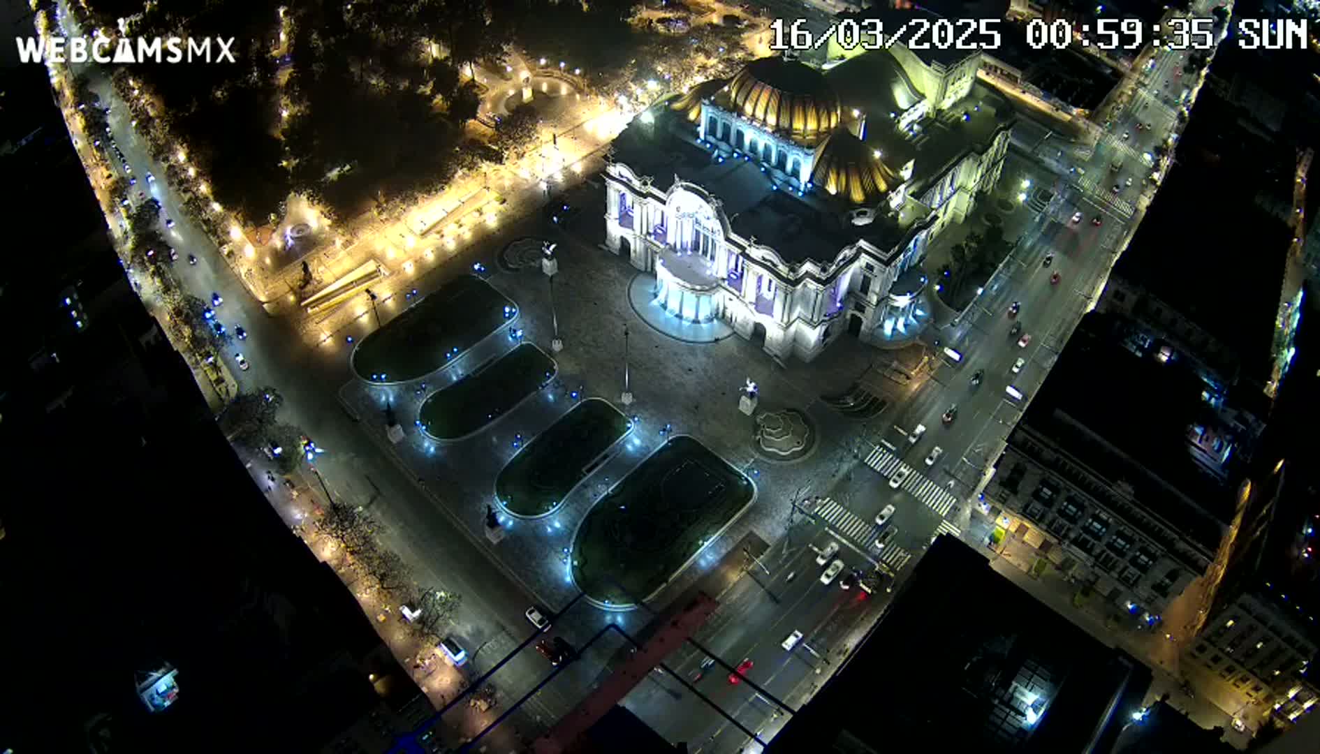An aerial nighttime view shows a large, illuminated building surrounded by streets and plazas with cars and landscaping.