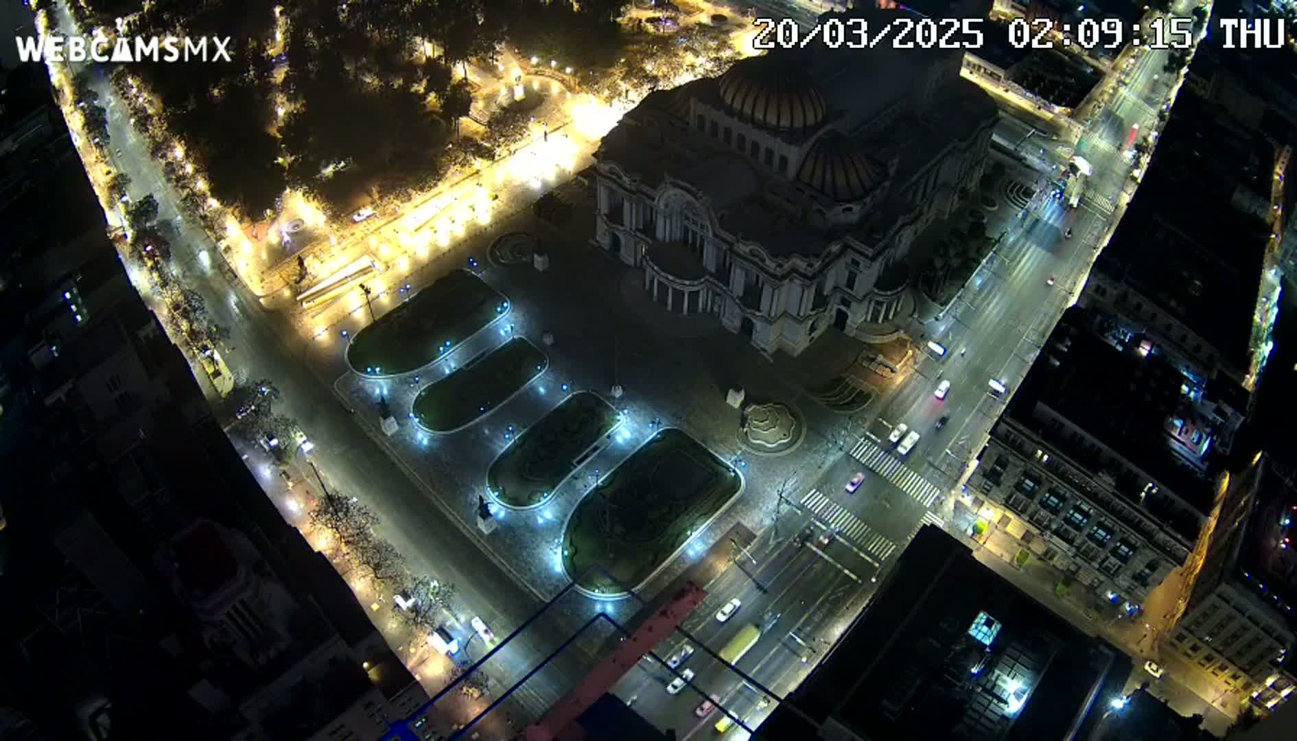 An illuminated Palacio de Bellas Artes and surrounding city streets at night are seen from an aerial perspective.
