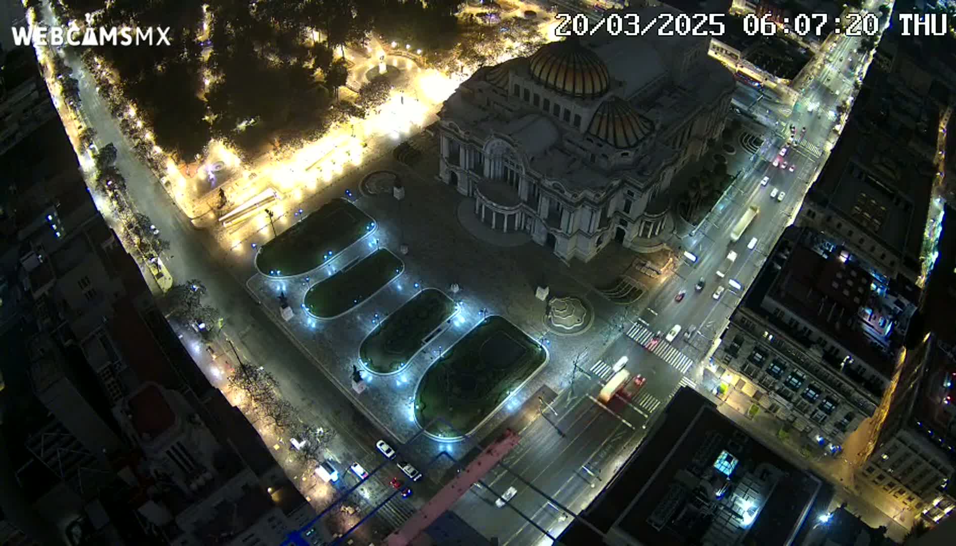 A nighttime aerial view shows a large building with a dome surrounded by a plaza with illuminated landscaping and streets with sparse traffic.