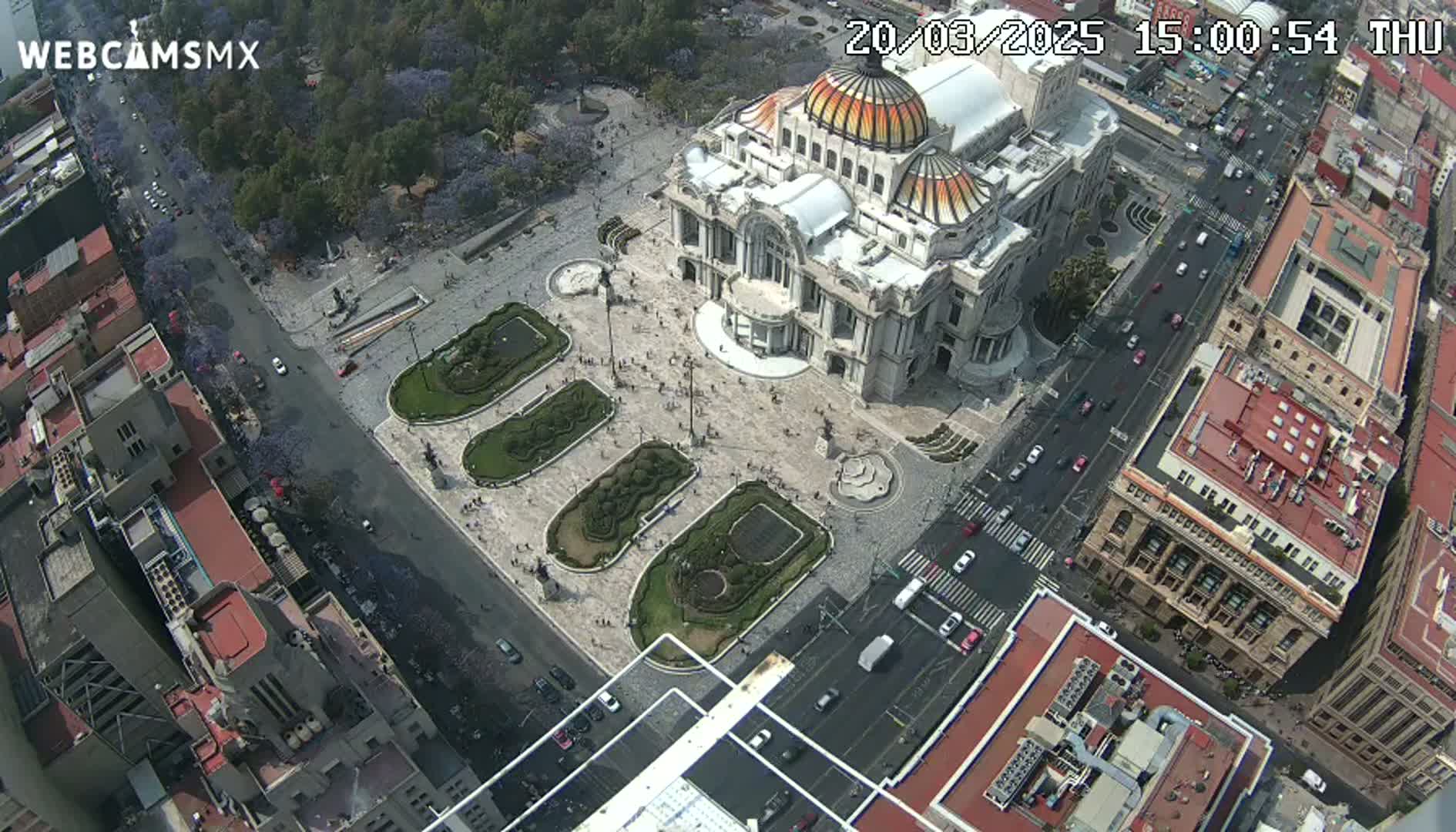 An aerial view shows a large plaza with a grand building in the center, surrounded by city streets and buildings on a clear day.