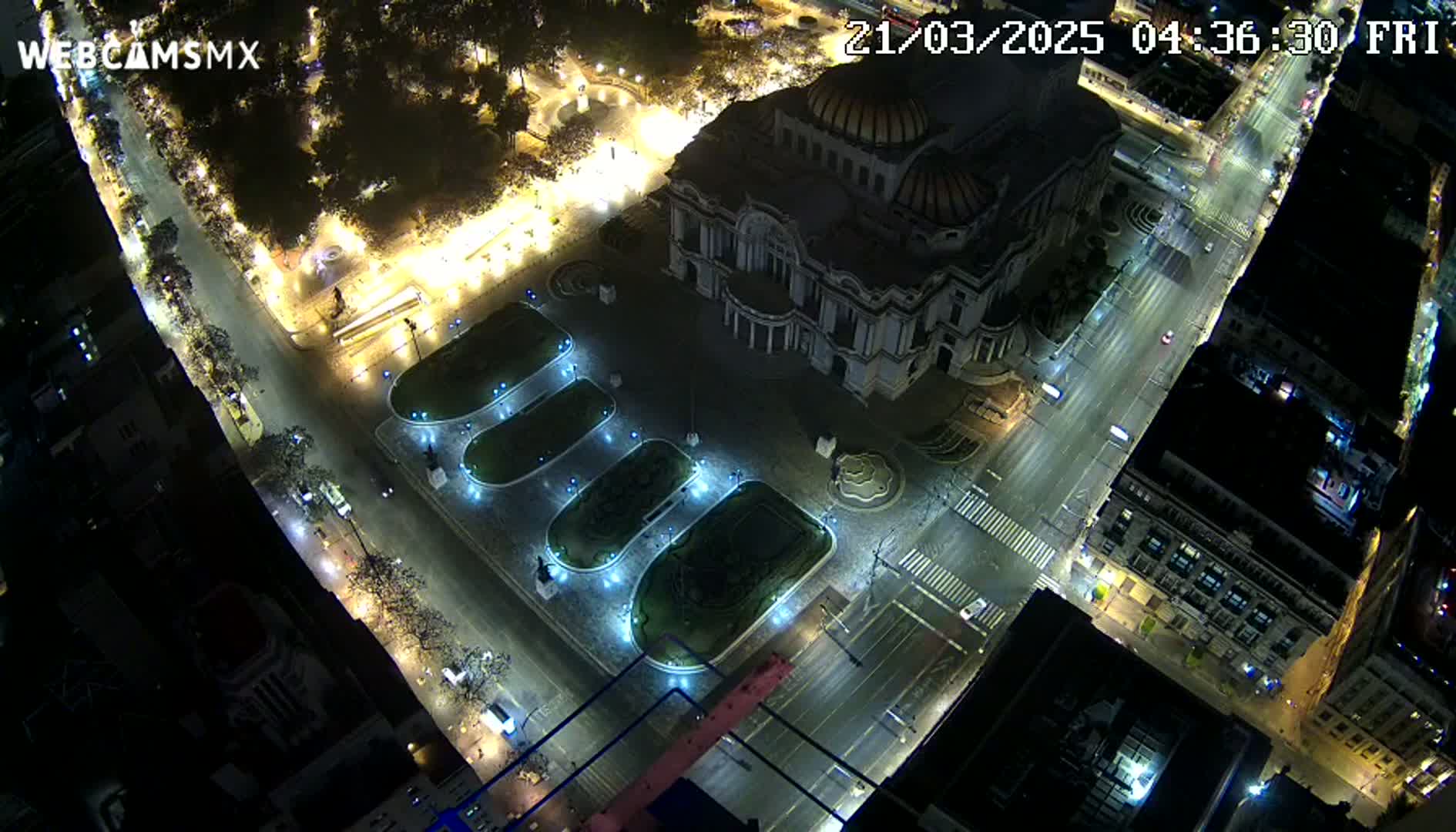 An aerial nighttime view shows a large building, possibly a museum, in a city square with sparsely trafficked streets and illuminated landscaping.