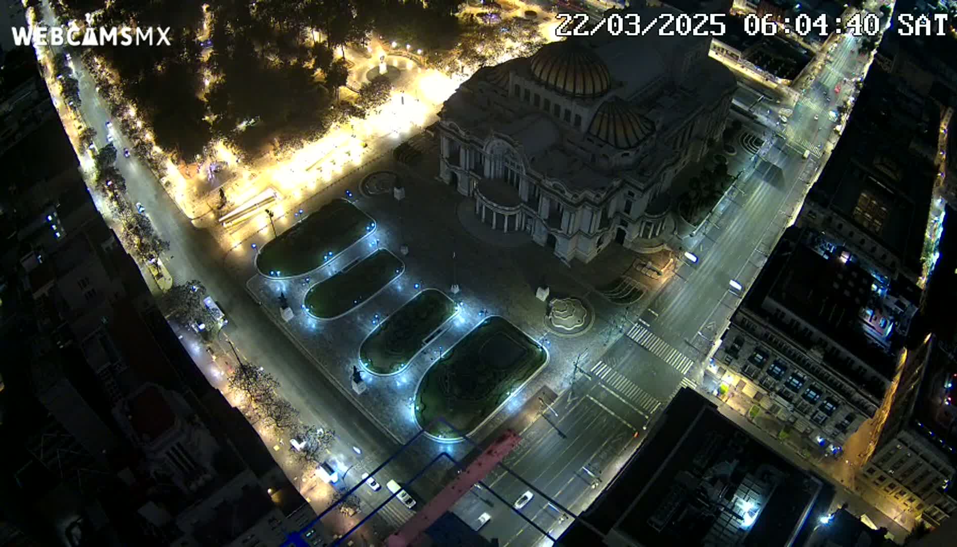 An aerial nighttime view of a large building with a dome, surrounded by a plaza with illuminated landscaping and streets with sparse traffic.