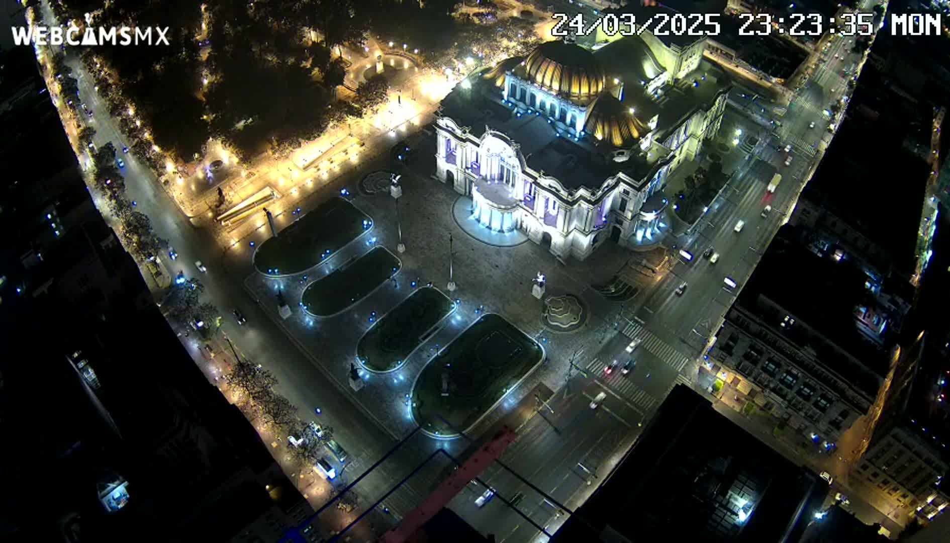 An aerial nighttime view shows a brightly lit palace surrounded by streets with cars and a plaza with landscaped areas.