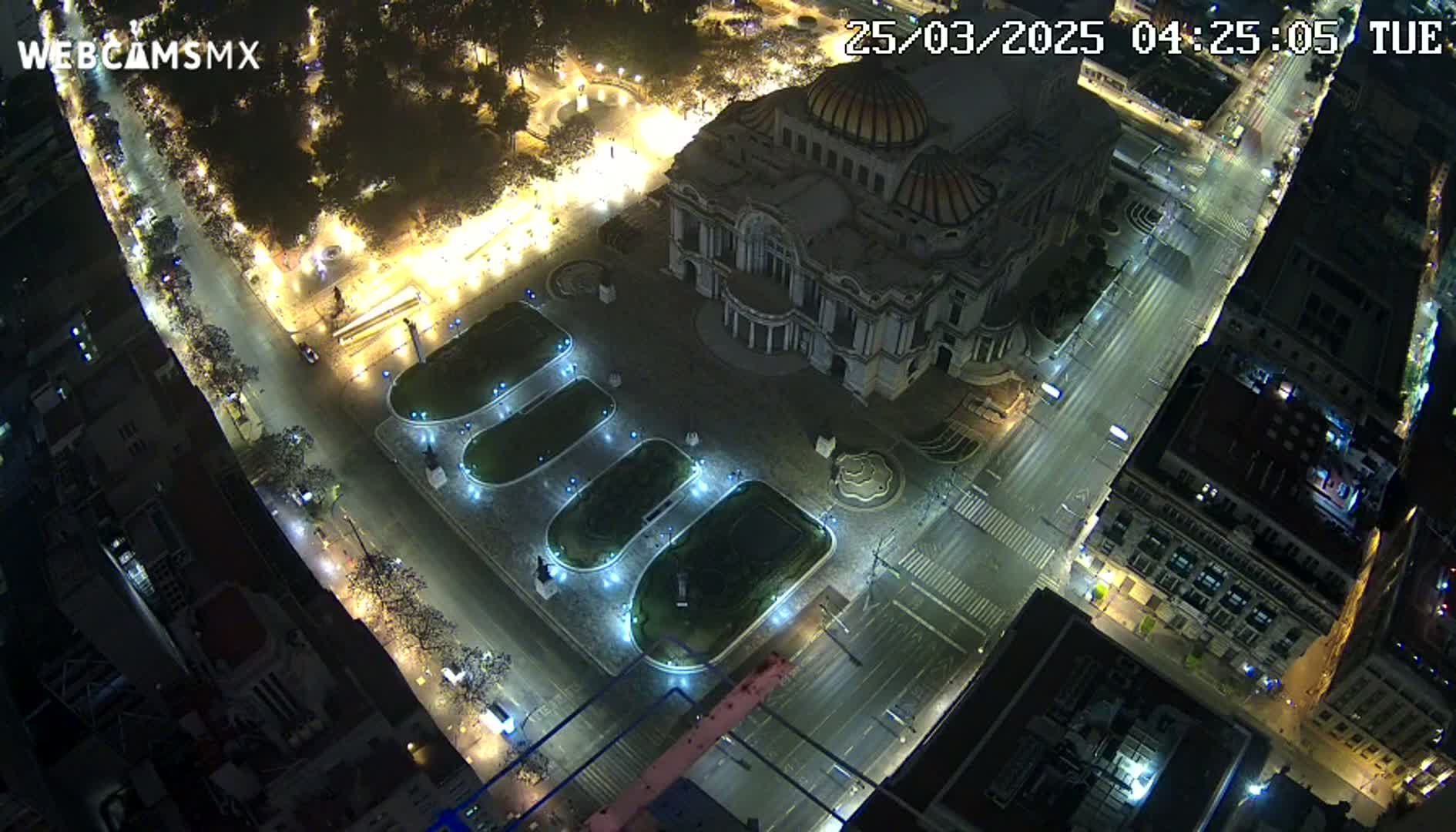 An aerial nighttime view of a city square with a large building, illuminated streets, and sparsely populated areas.