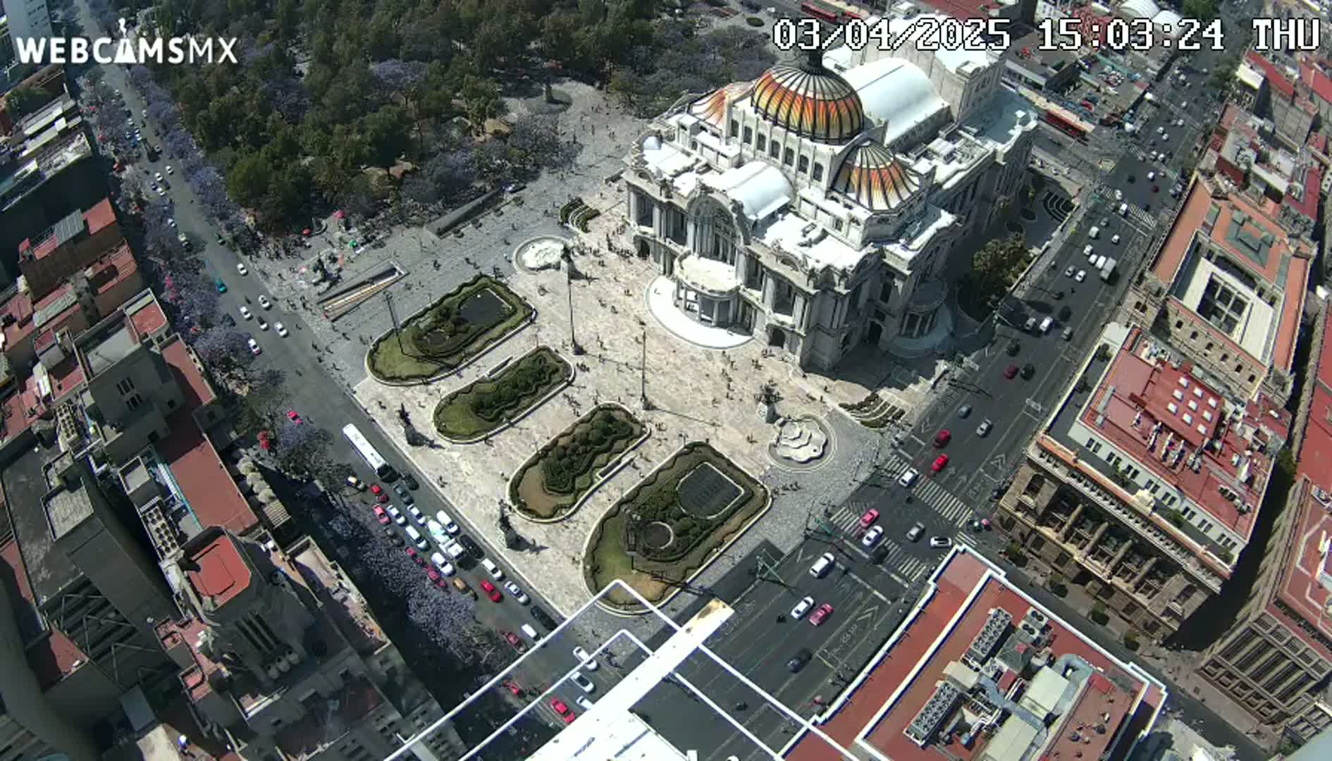 An aerial view shows a large, ornate building in a city square surrounded by streets with cars and buildings on a sunny day.