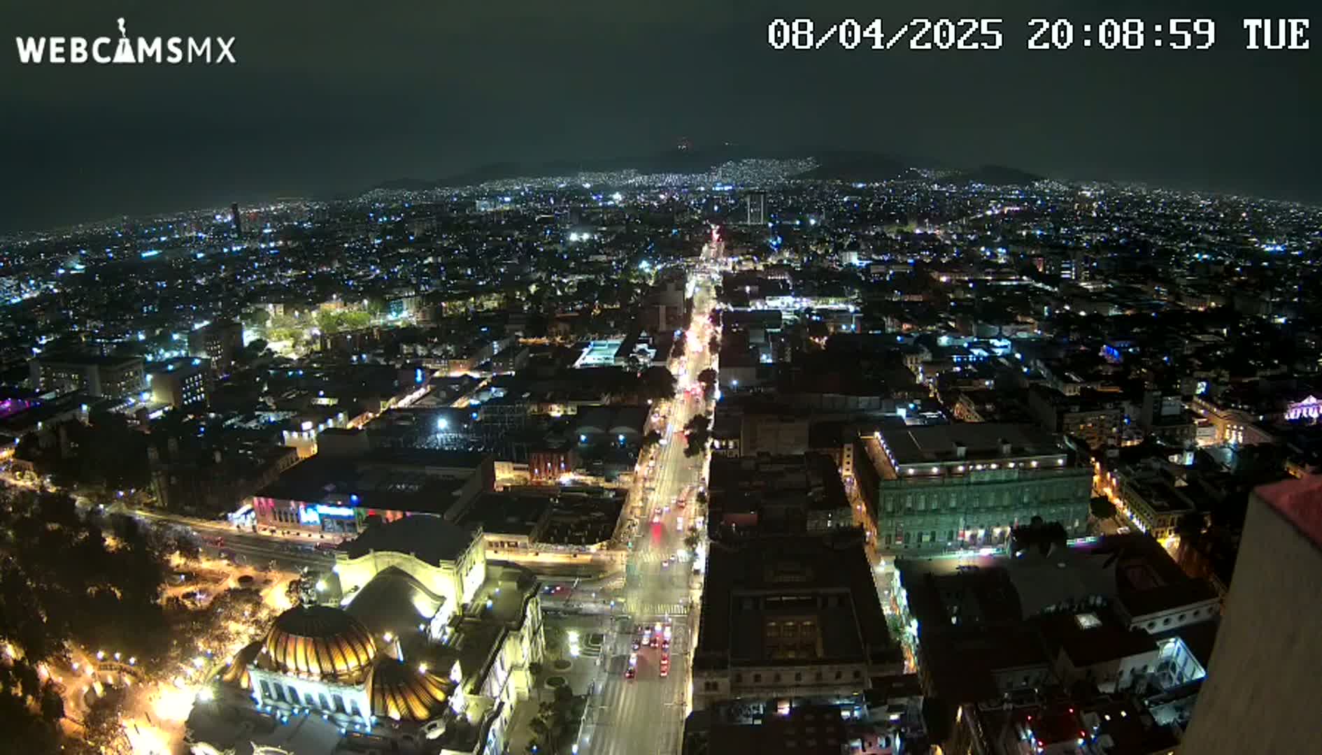 A nighttime aerial view of a city with brightly lit streets and buildings, under a clear sky.