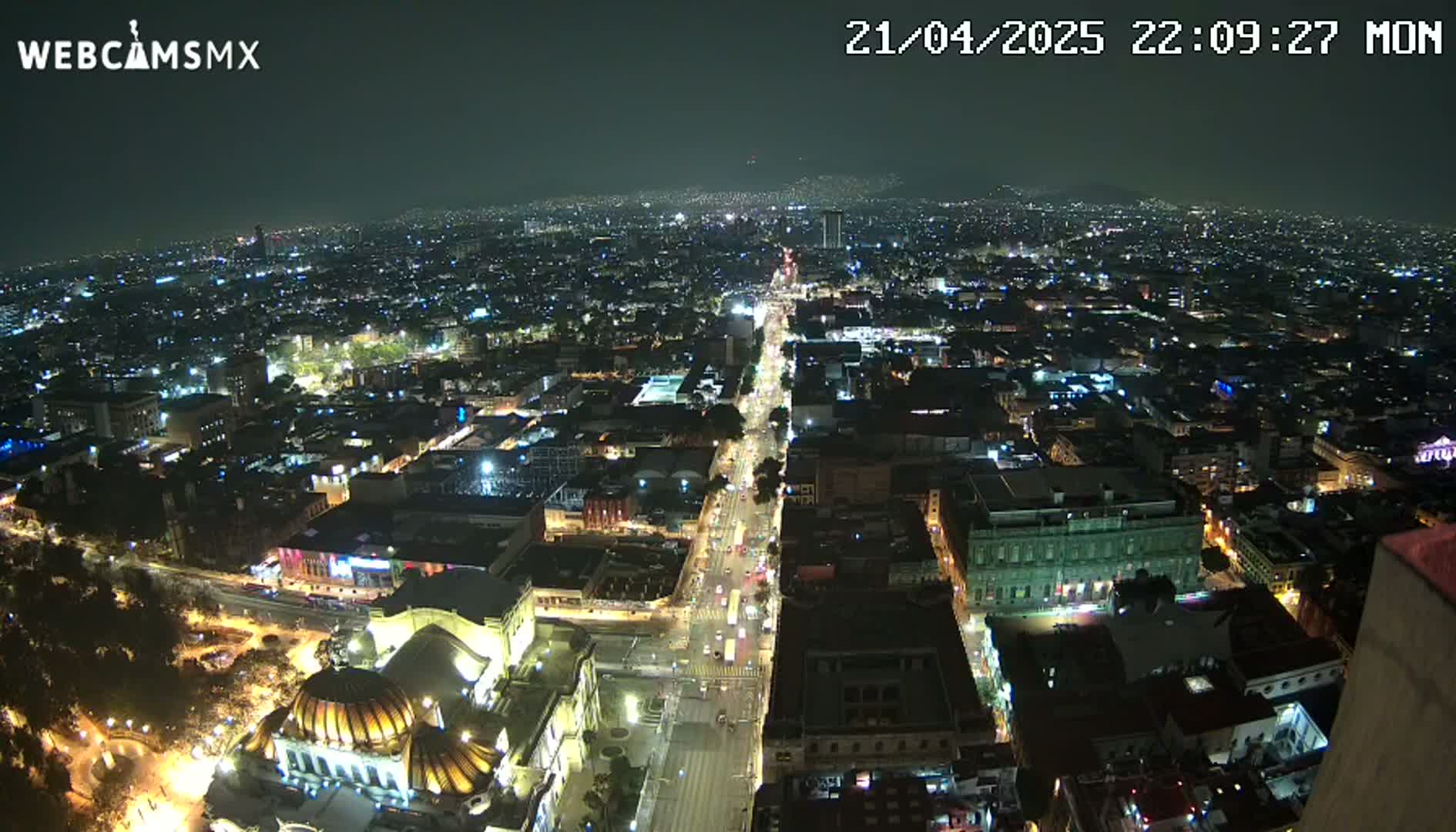 A nighttime, high-angle view of a sprawling city with brightly lit streets and buildings.