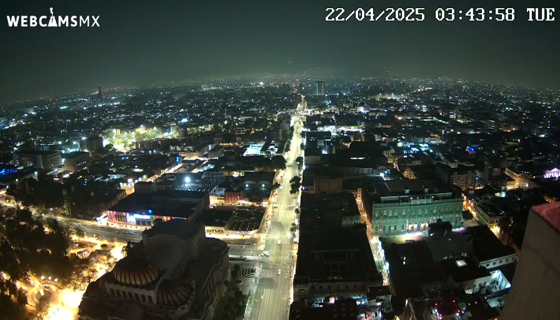 A nighttime, high-angle view shows a sprawling city illuminated by streetlights and building lights, with a long, brightly lit avenue cutting through the urban landscape.