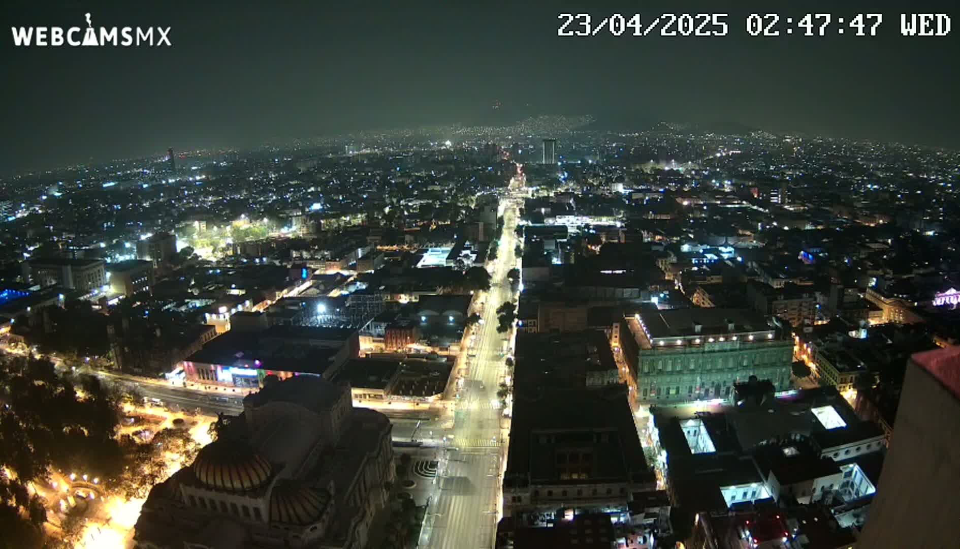 A nighttime, high-angle view shows a sprawling city with brightly lit streets and buildings under a clear, dark sky.