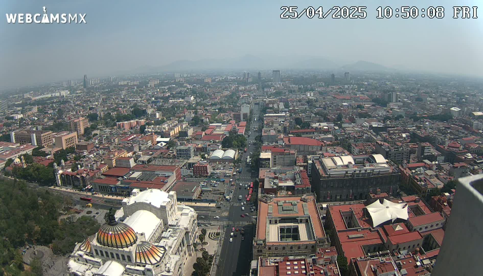 A hazy, high-angle view of a sprawling city shows a wide avenue lined with buildings, culminating in a large domed structure at the bottom.
