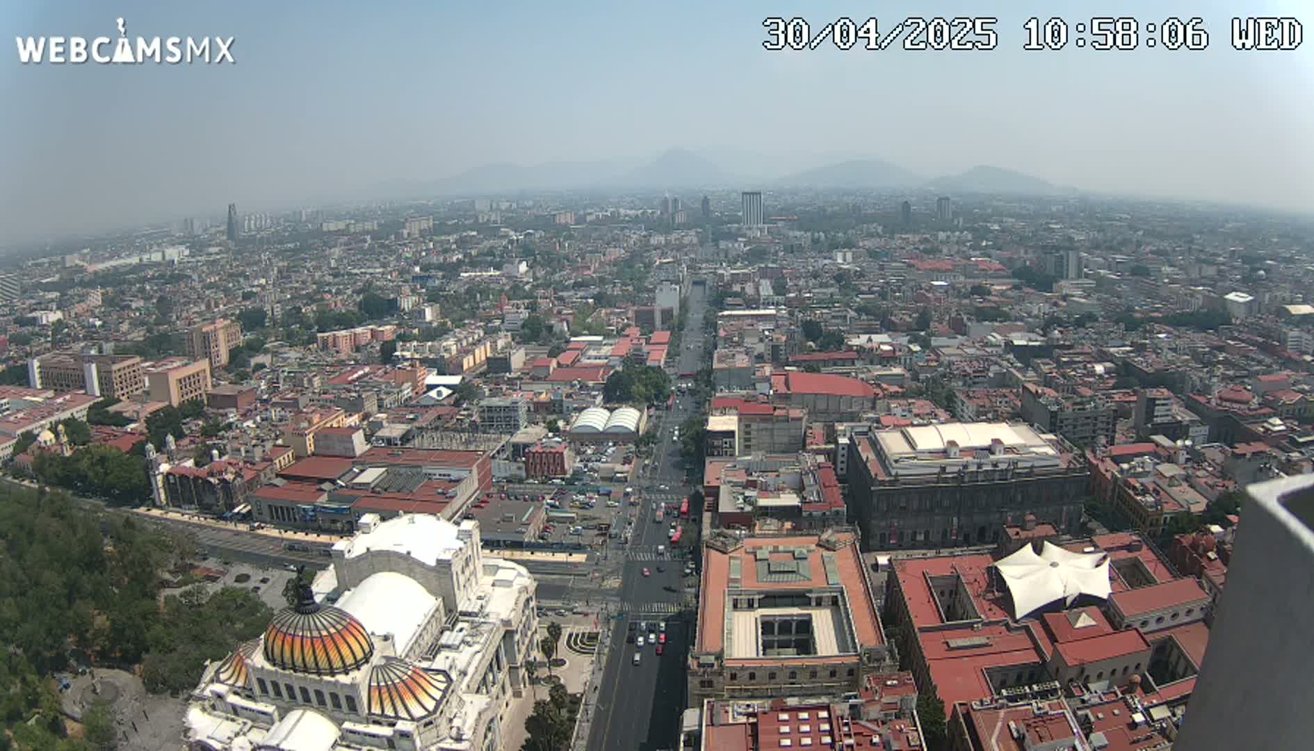 A hazy, high-angle view shows a sprawling city with red-tiled rooftops and a wide avenue, culminating in a large domed building.