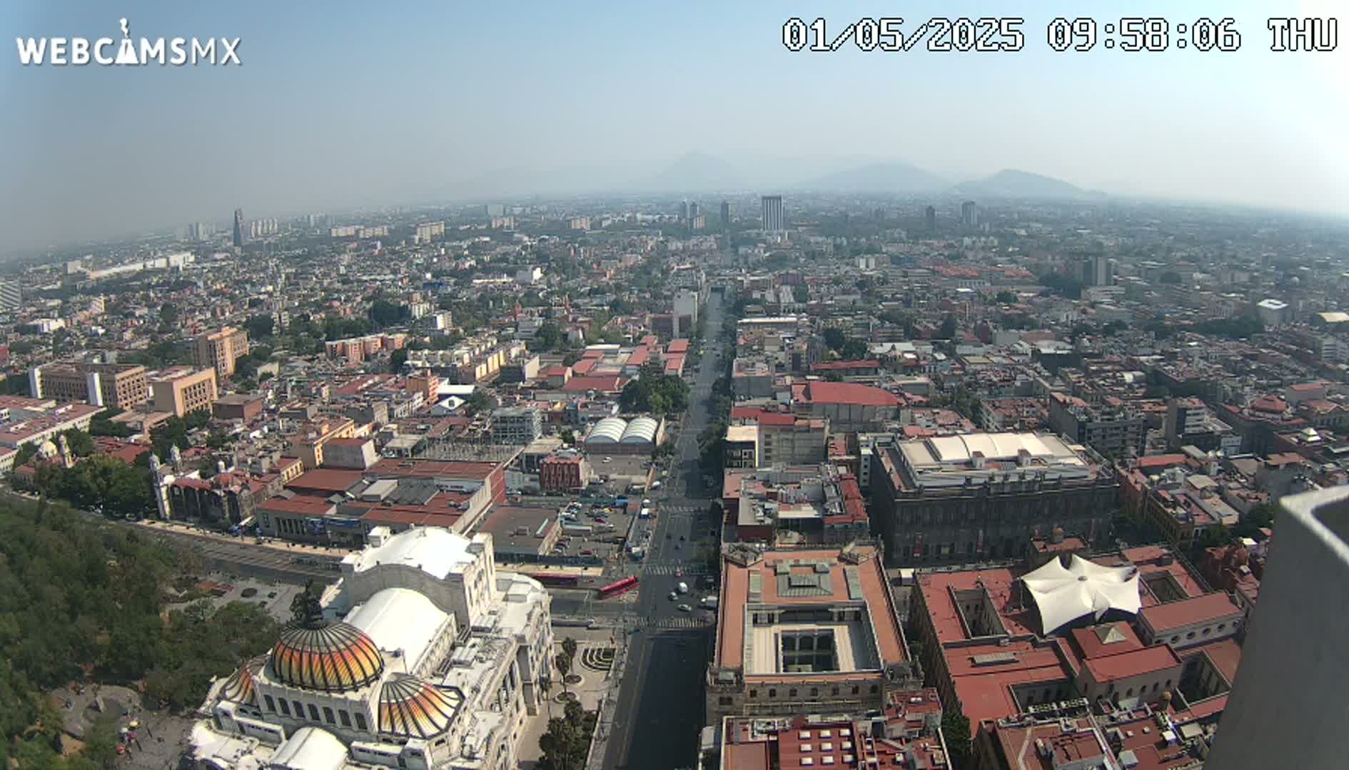A hazy, high-angle view shows a vast cityscape extending to distant mountains under a clear sky.
