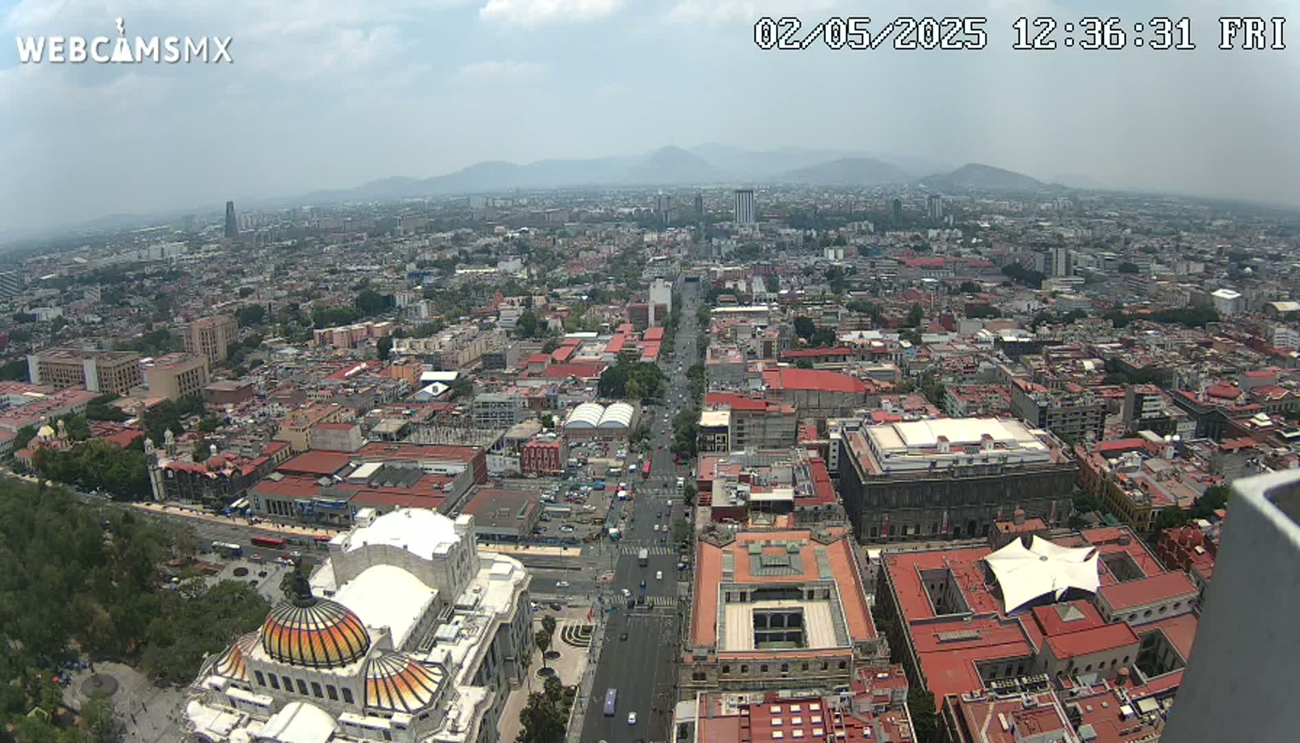 A hazy, high-angle view shows a sprawling city with a long, wide avenue cutting through it, leading to distant mountains.
