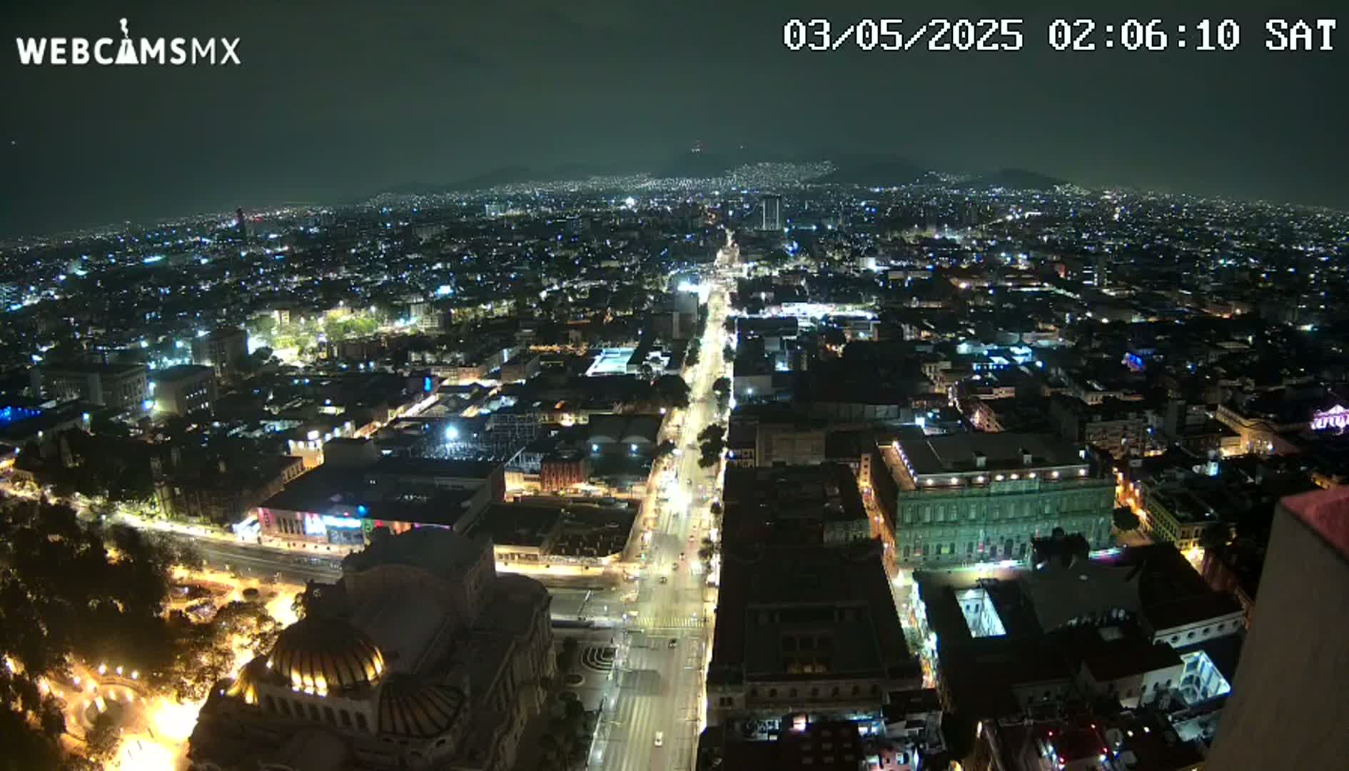 A nighttime, high-angle view shows a sprawling city illuminated by streetlights and building lights, with a long, brightly lit avenue cutting through the urban landscape.