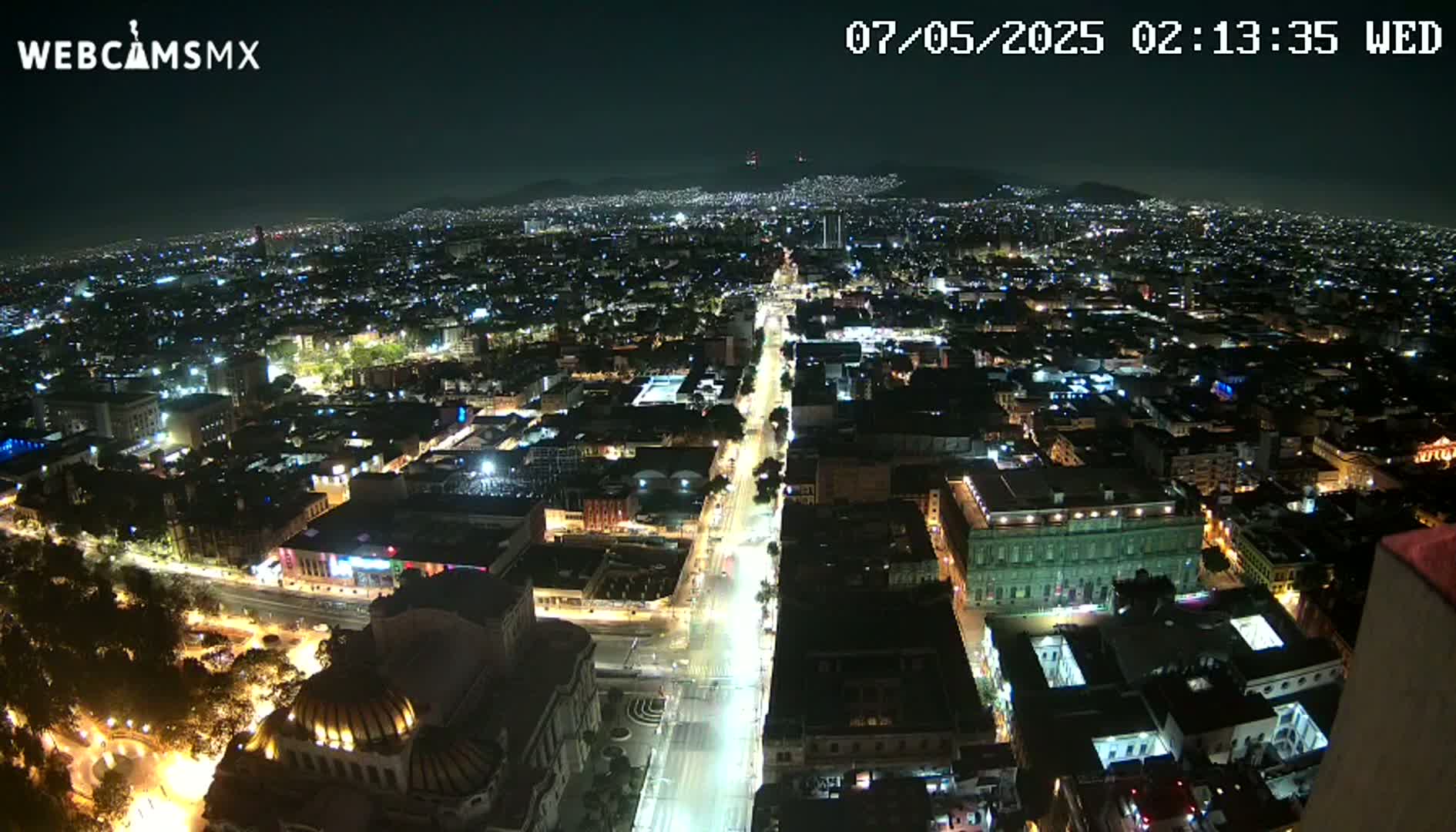 A nighttime aerial view shows a sprawling city with brightly lit streets and buildings under a clear sky.