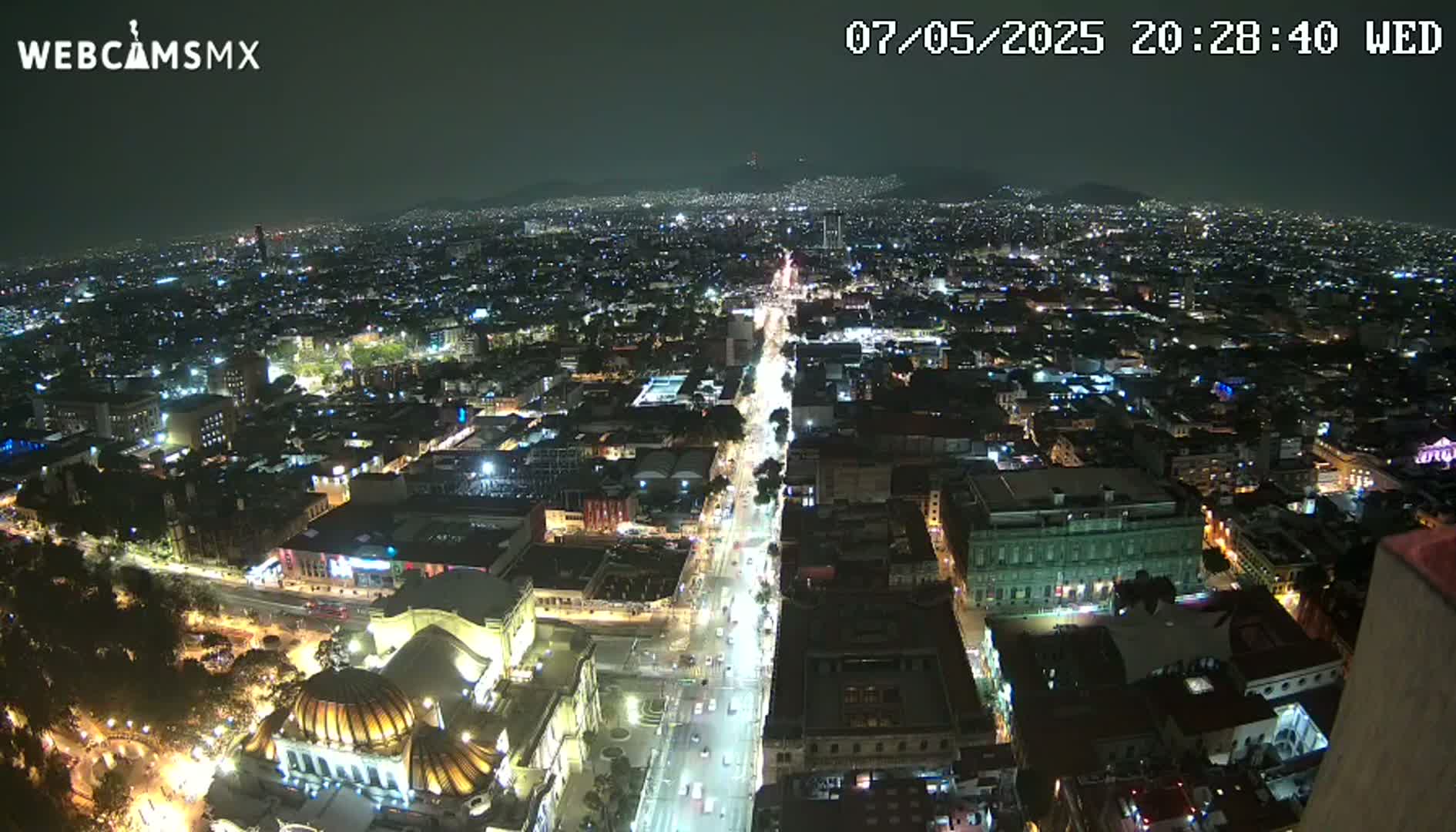 A nighttime aerial view shows a sprawling city with brightly lit streets and buildings under a clear sky.