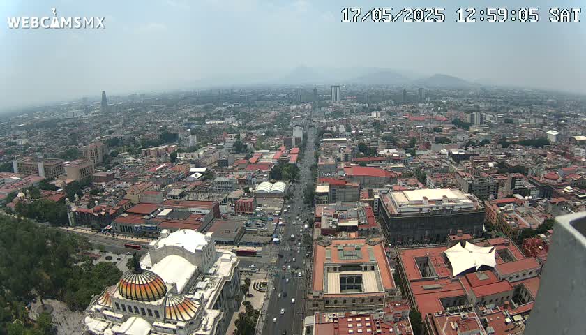 A hazy, high-angle view of a sprawling city, showing a wide avenue cutting through numerous buildings, culminating in a large, ornate dome-topped structure in the foreground.