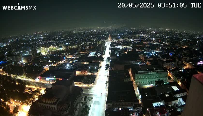 A nighttime aerial view of a city, showing brightly lit streets and buildings under hazy conditions.