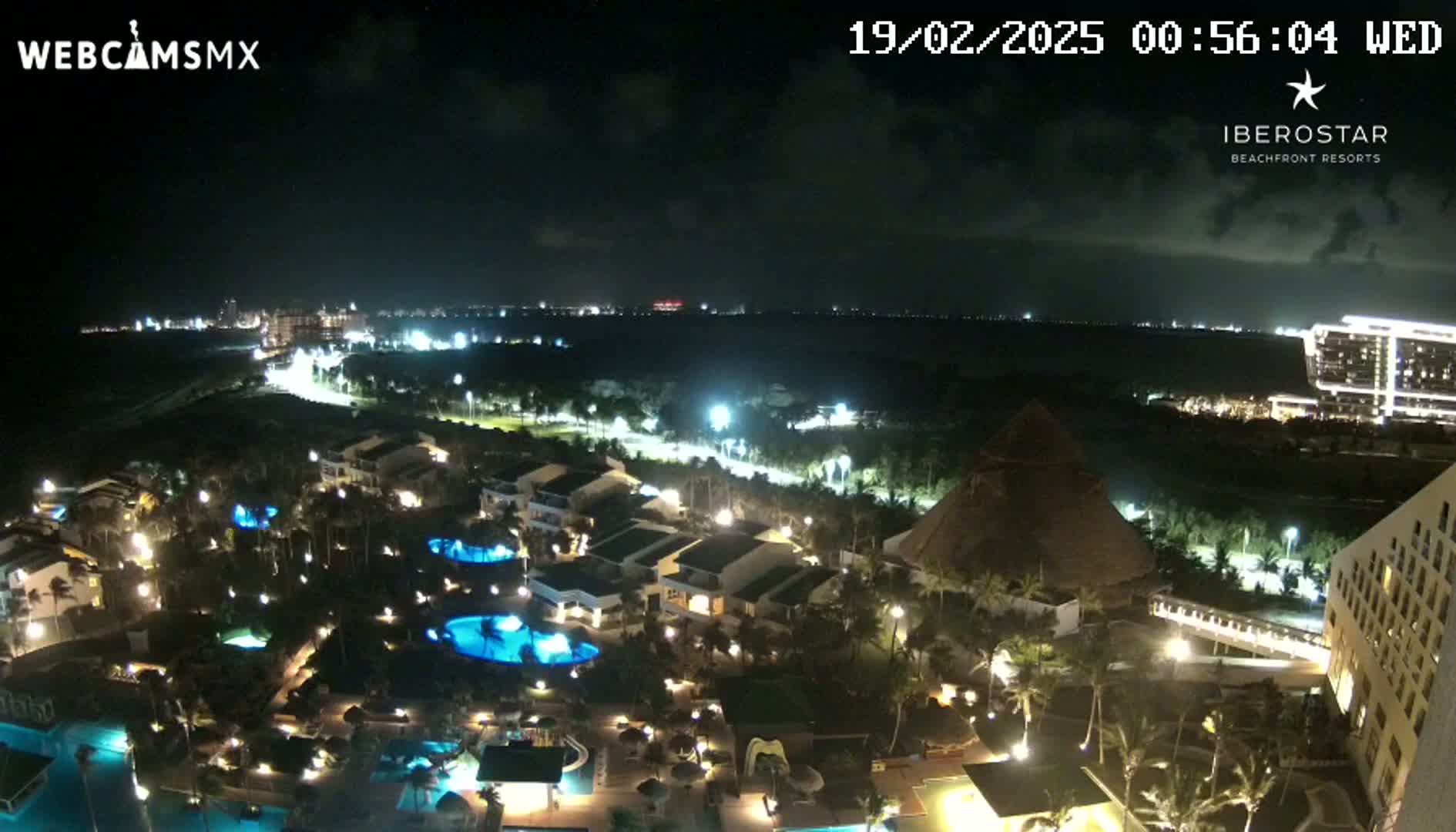A nighttime view of a resort complex with illuminated buildings, pools, and landscaping, under a mostly clear sky.