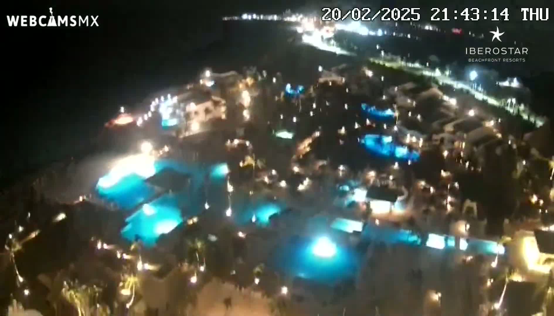 An aerial nighttime view shows numerous illuminated swimming pools and buildings at a resort.