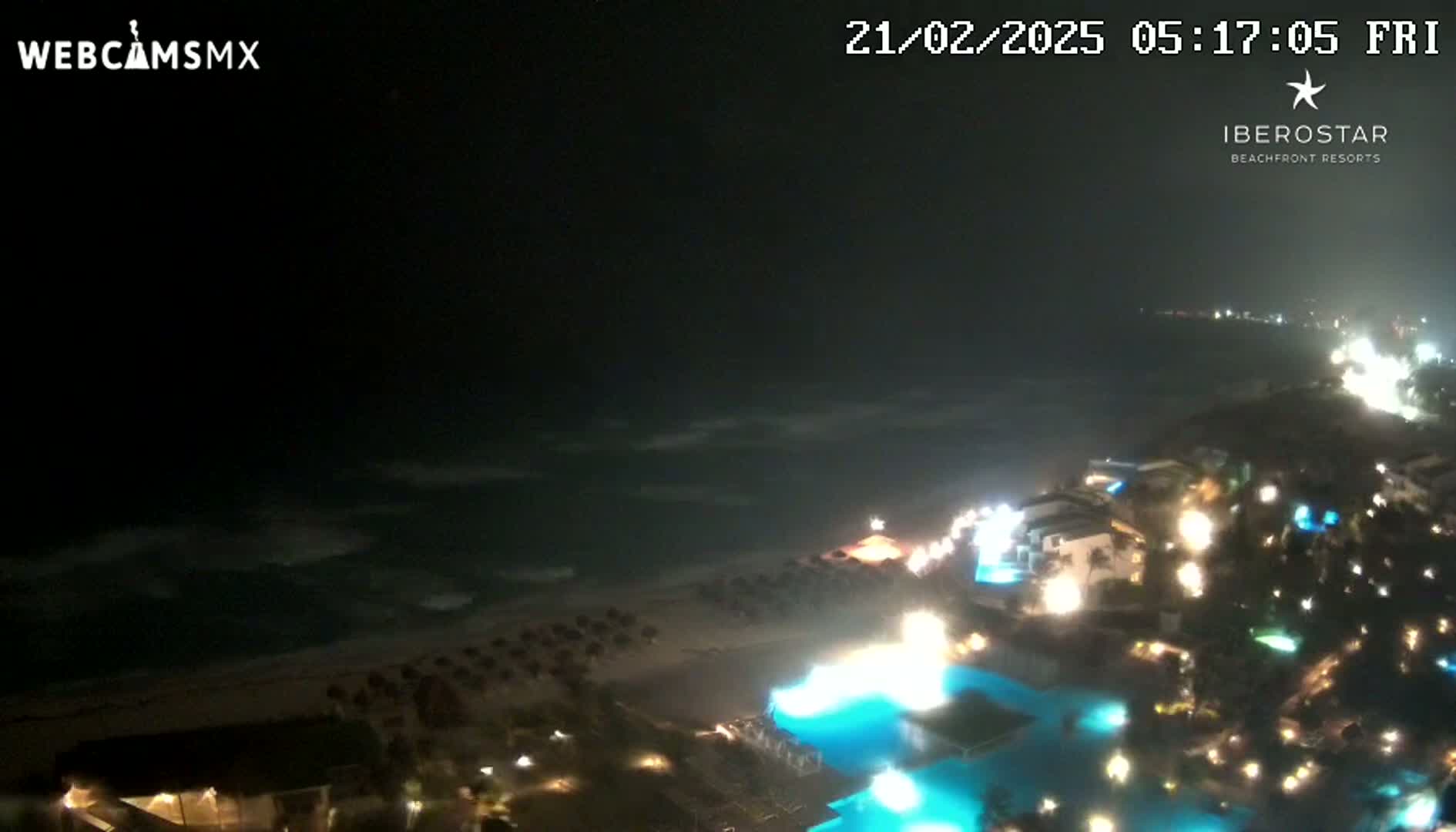 A nighttime view of a resort town on a beach with gently waving ocean waters under a dark sky.
