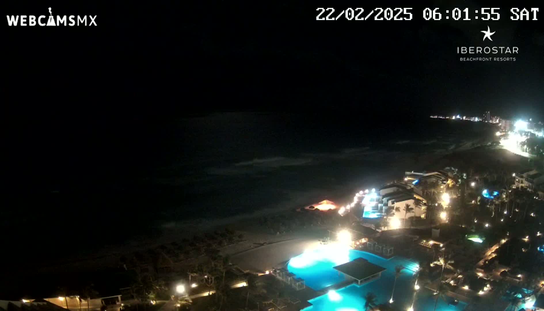 A nighttime aerial view of a resort on a beach, with dark ocean waves visible under a clear night sky.