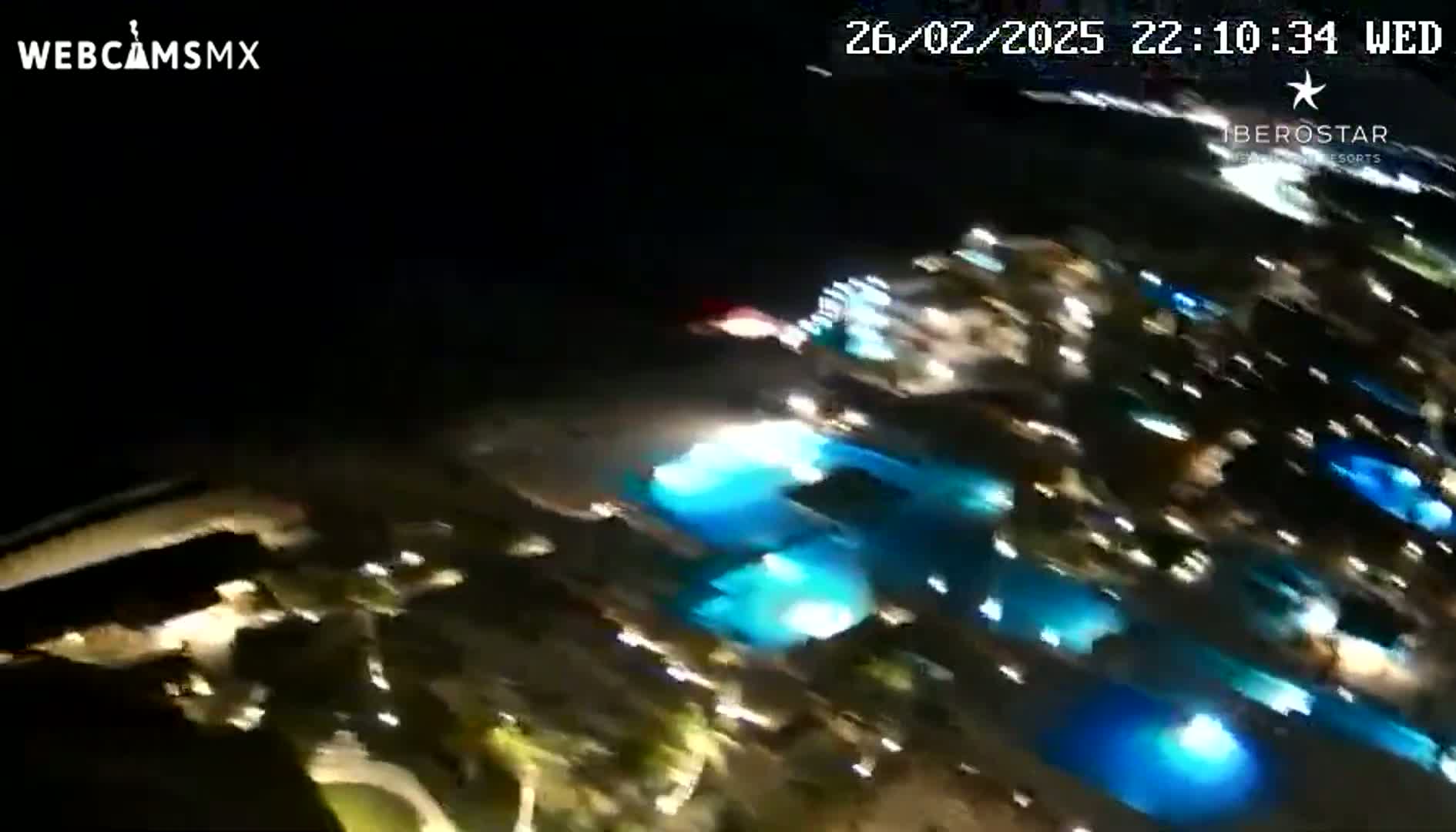 A blurry nighttime aerial view shows brightly lit resort buildings and pools.