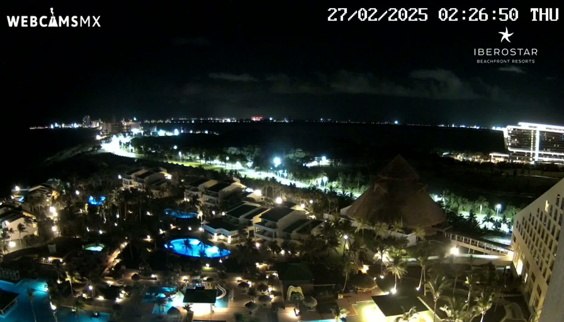 A nighttime aerial view of a resort complex with illuminated buildings, pools, and landscaping, under a mostly clear sky.