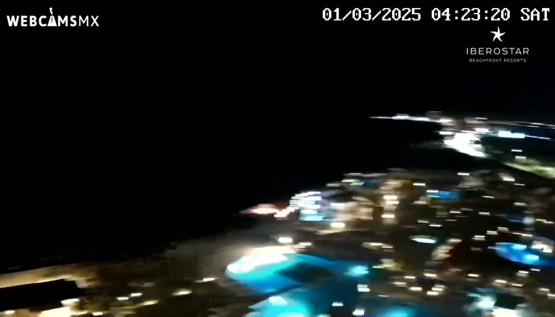 A blurry nighttime aerial view shows brightly lit buildings and pools of water.