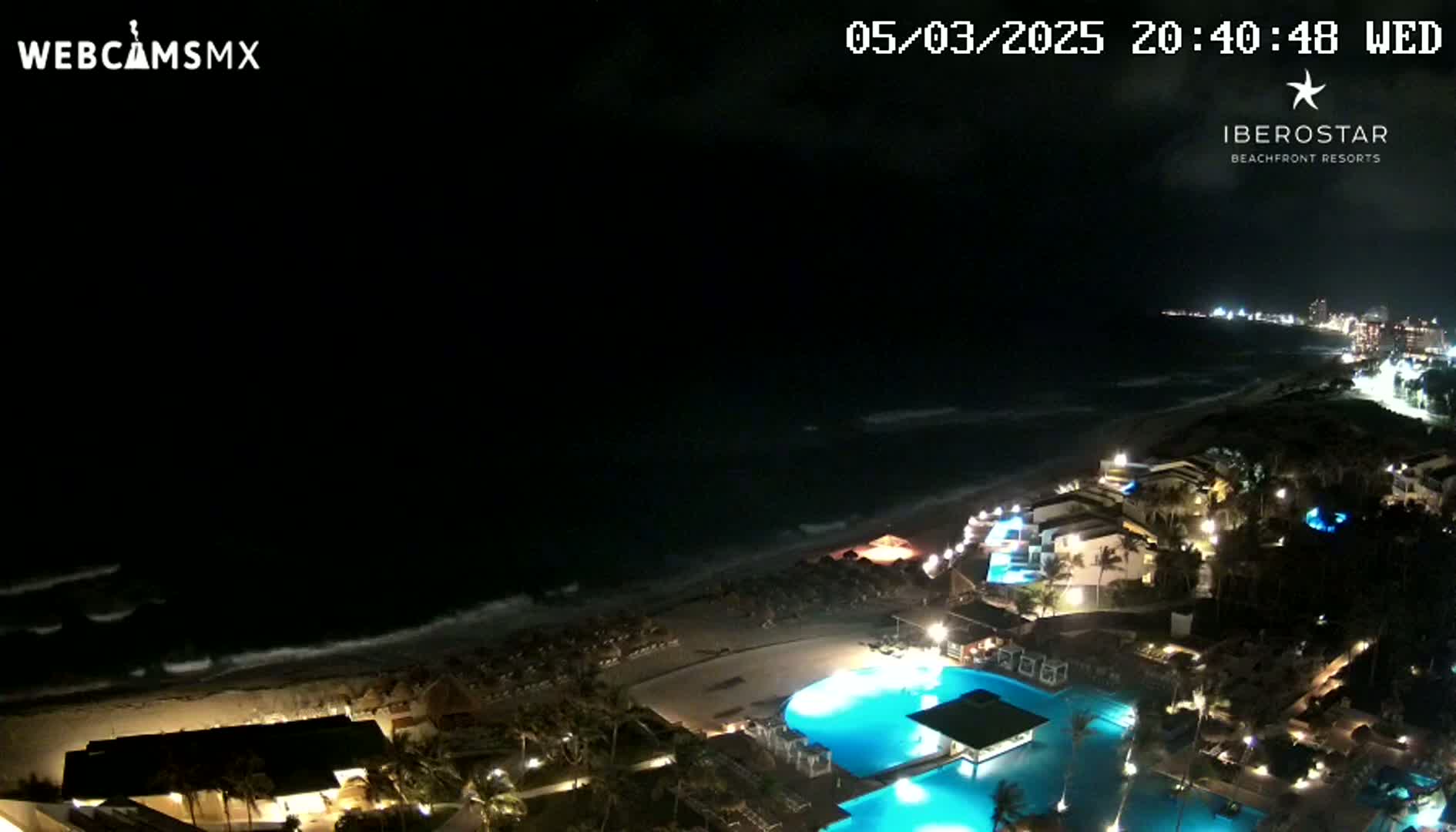 A nighttime view of a resort on a beach with gently crashing waves under a dark sky.