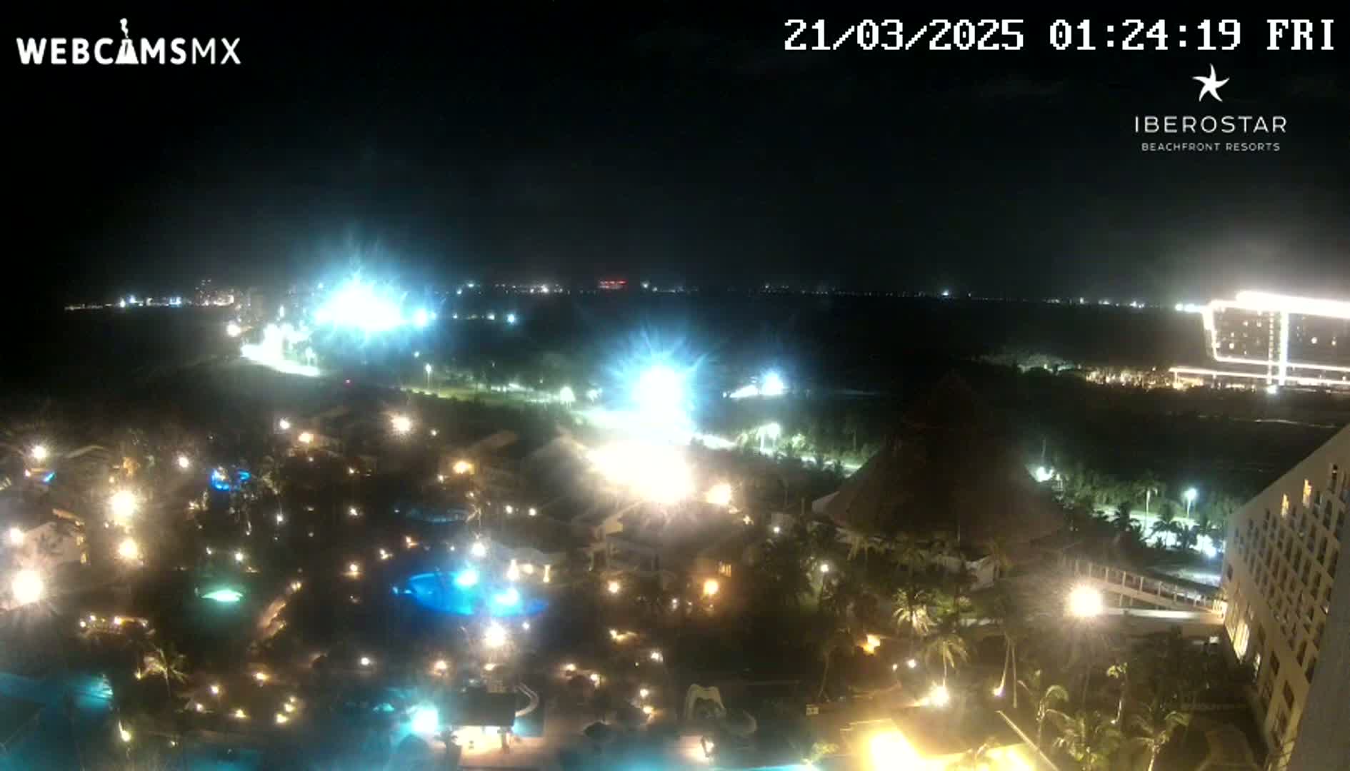 A nighttime, high-angle view of a brightly lit resort complex near a coastline, under a clear sky.