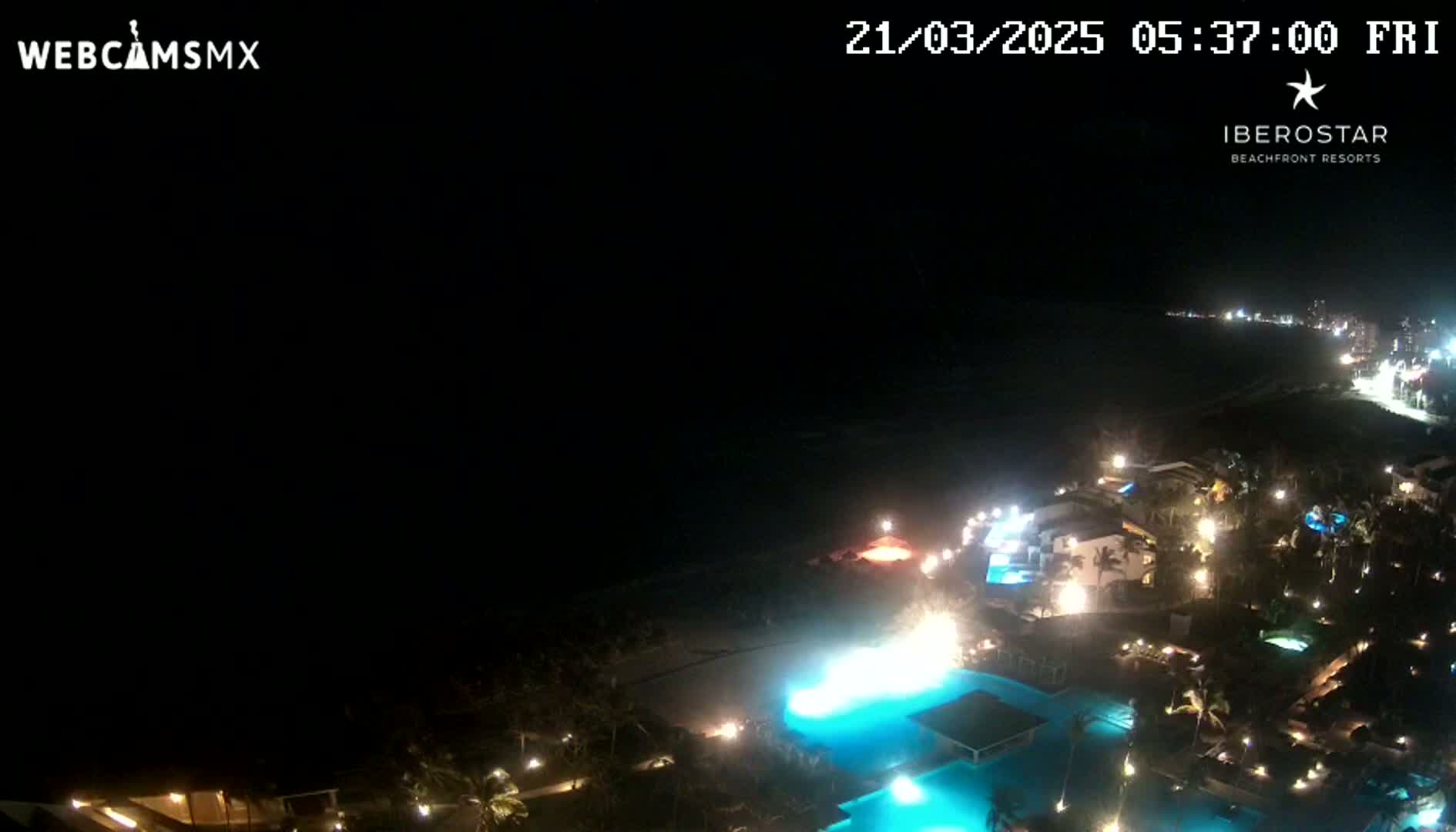 A nighttime aerial view shows a resort complex illuminated near a dark ocean under a clear sky.