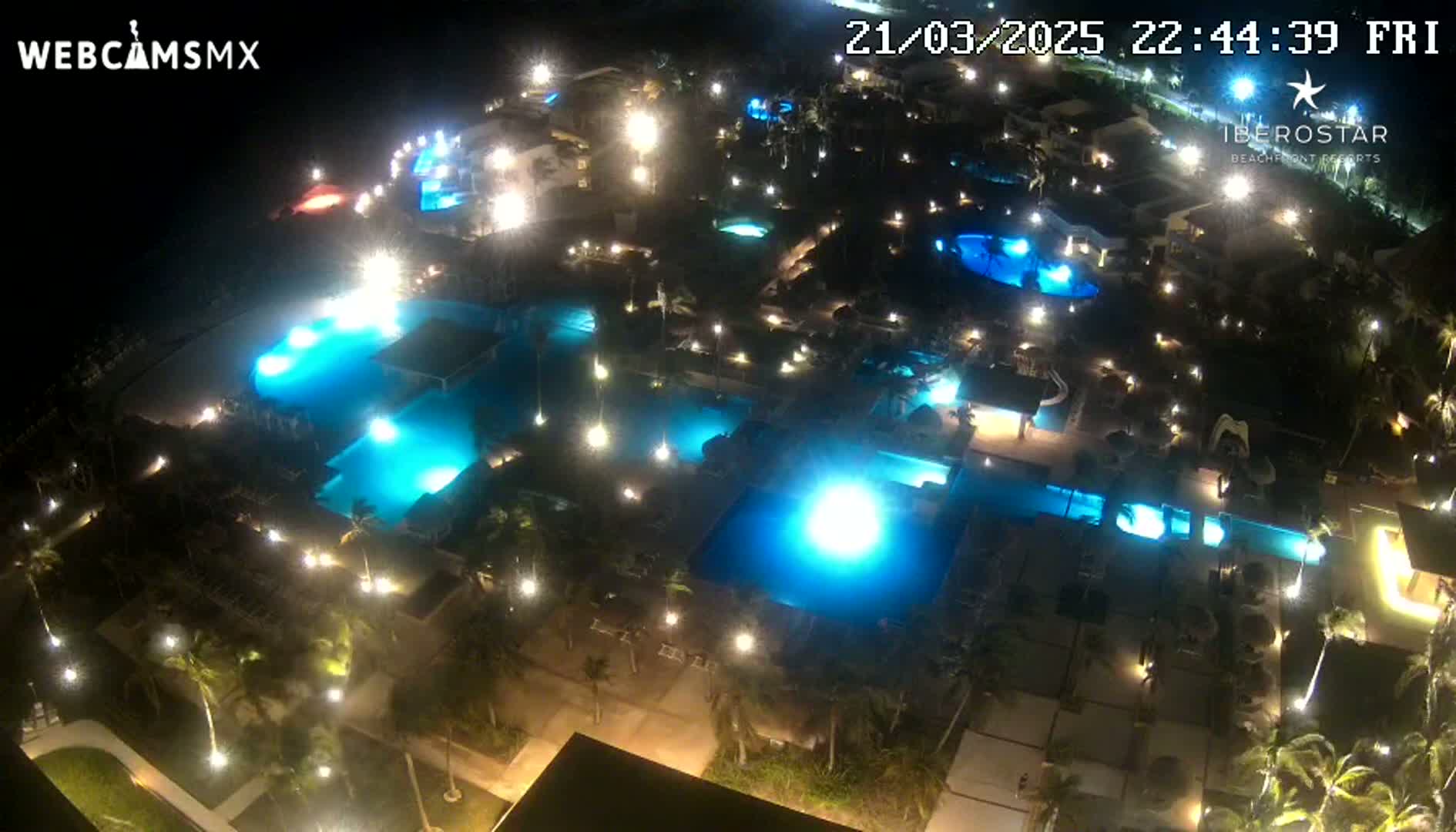 An aerial nighttime view of a resort complex with numerous illuminated swimming pools and surrounding landscaping.