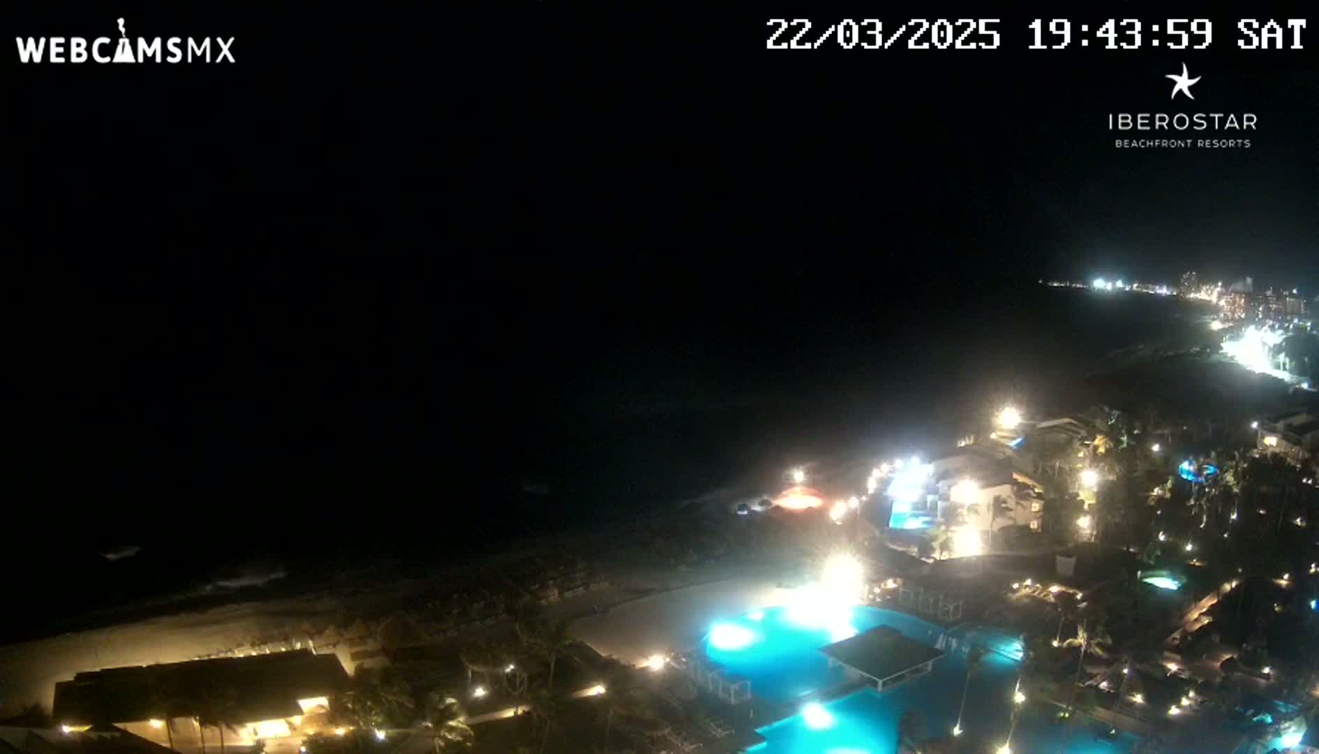 A nighttime, high-angle view of a resort complex illuminated along a dark ocean shoreline.
