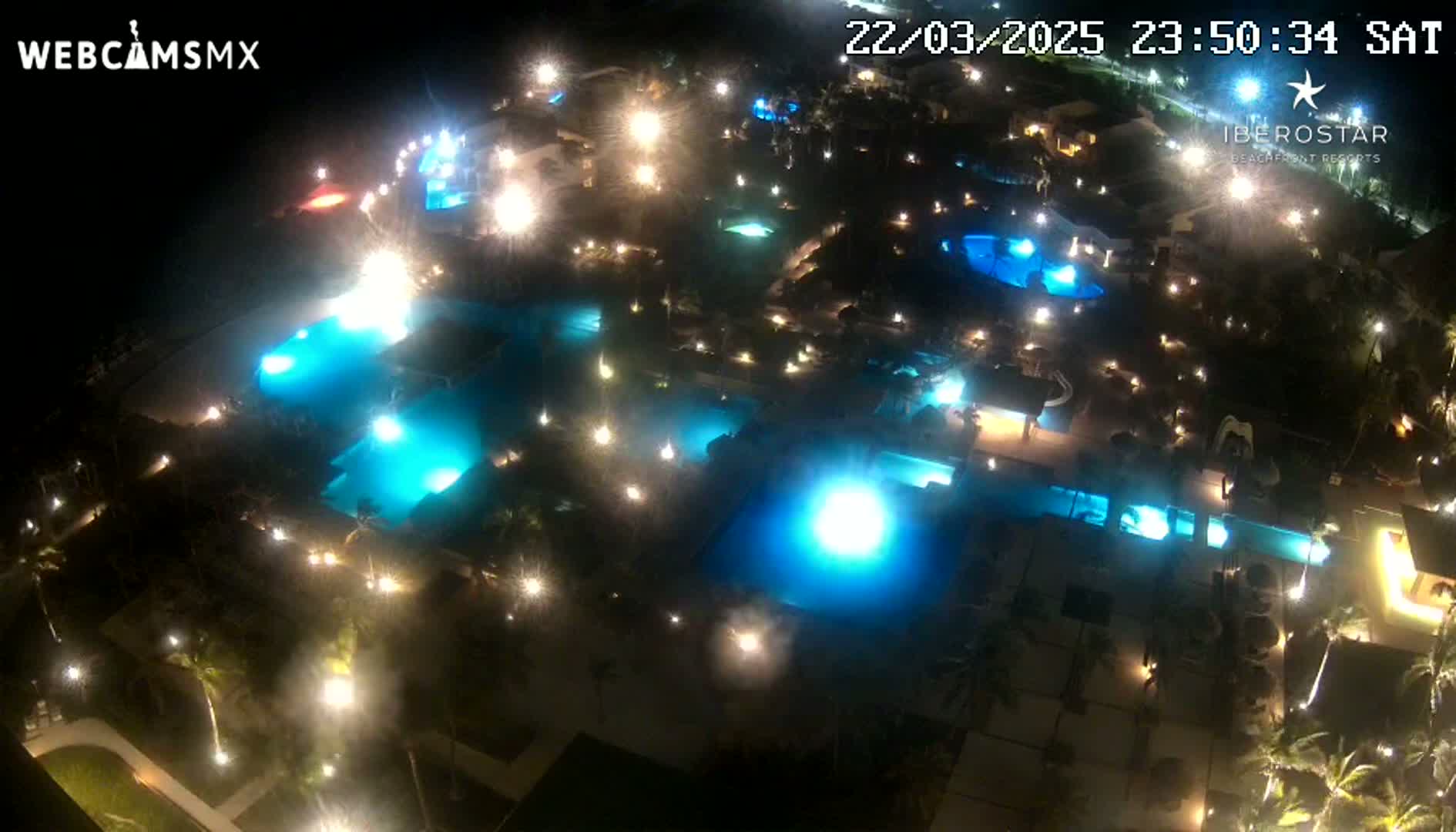 A nighttime aerial view of a resort complex featuring numerous illuminated swimming pools and landscaping.