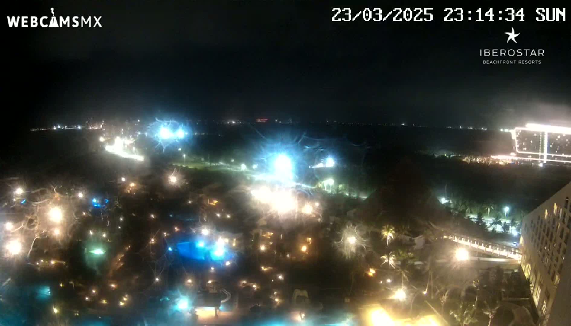 A nighttime aerial view of a resort complex with brightly lit pools and buildings, under a clear sky.