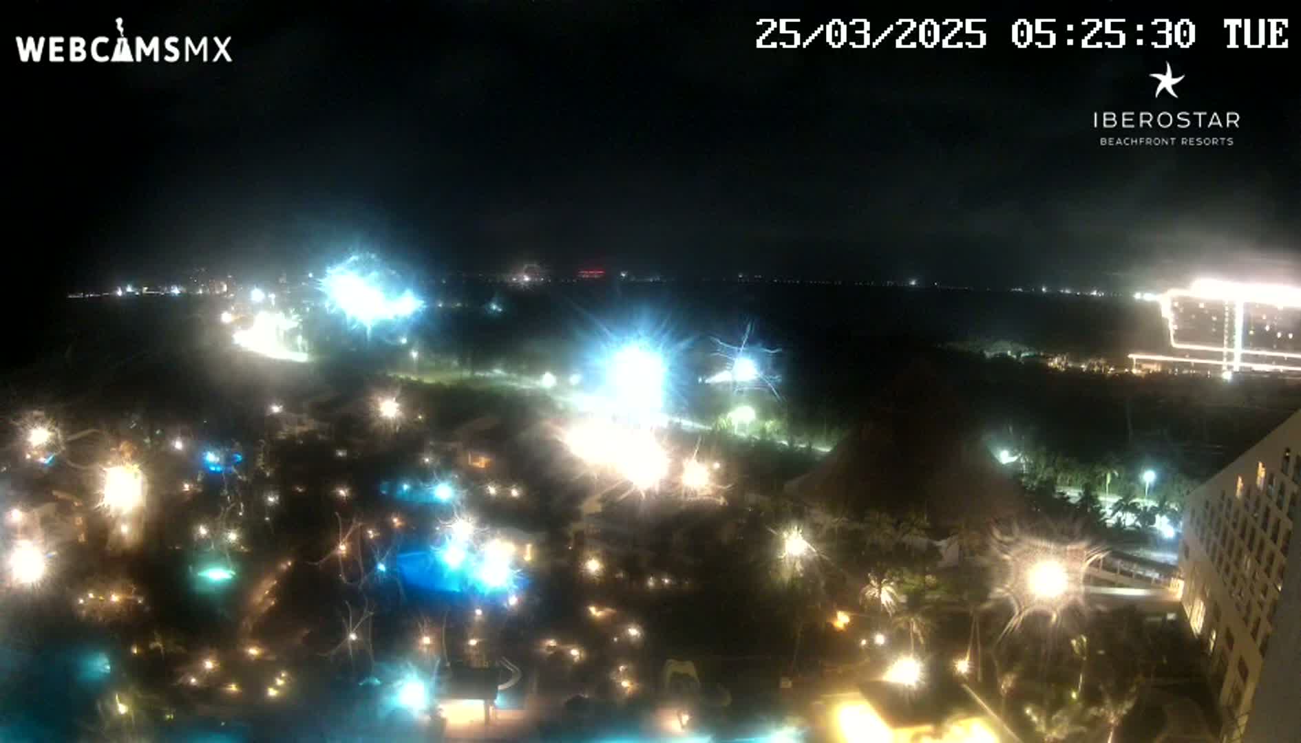 A nighttime aerial view of a resort area with brightly lit pools and buildings, under a clear, dark sky.