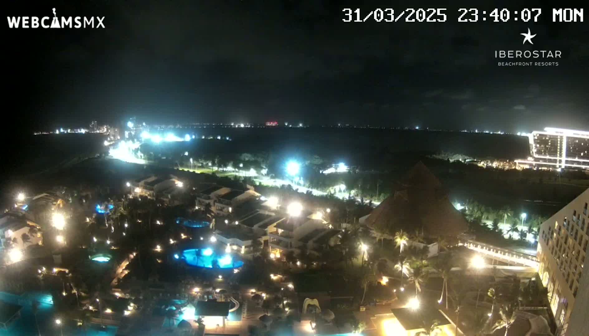 A nighttime aerial view of a resort complex with illuminated buildings, pools, and landscaping, under a clear, dark sky.