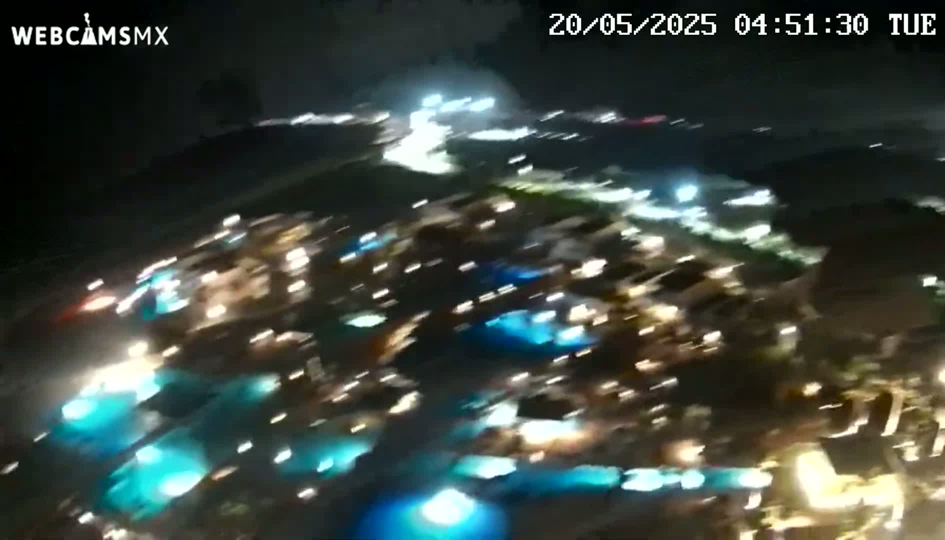 A nighttime aerial view shows numerous illuminated buildings and pools of water.