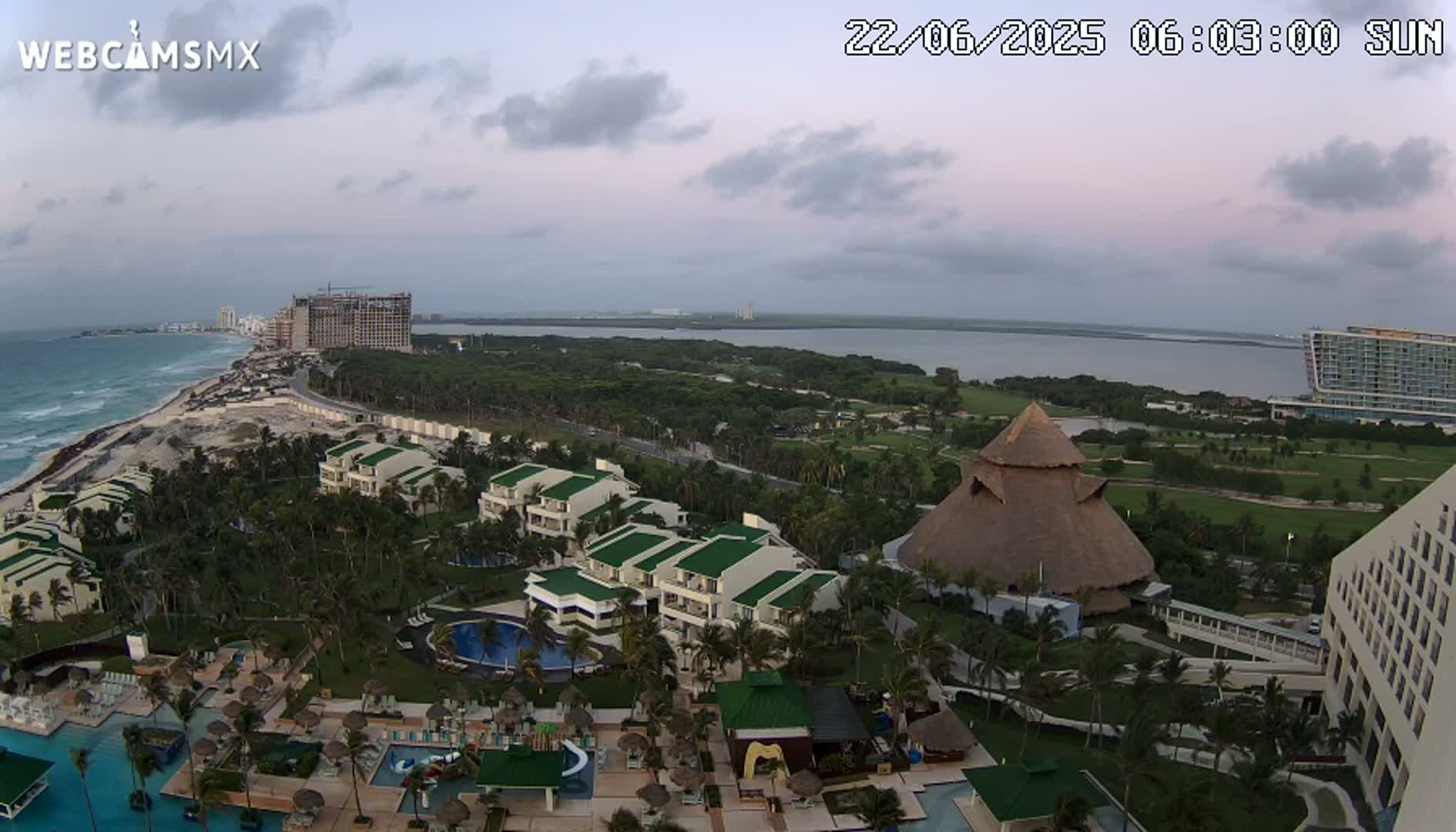 An aerial view of a resort complex on a coast, with a body of water and partly cloudy skies.