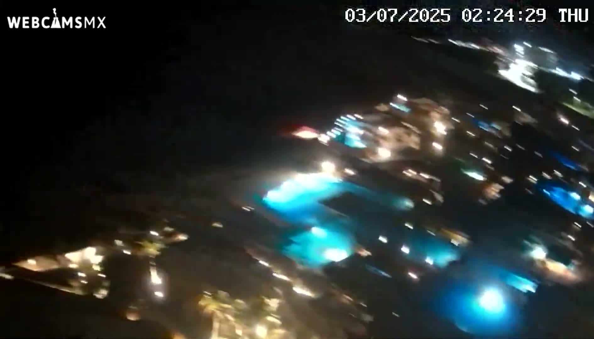 A blurry nighttime image shows brightly lit buildings and pools of blue-lit water.