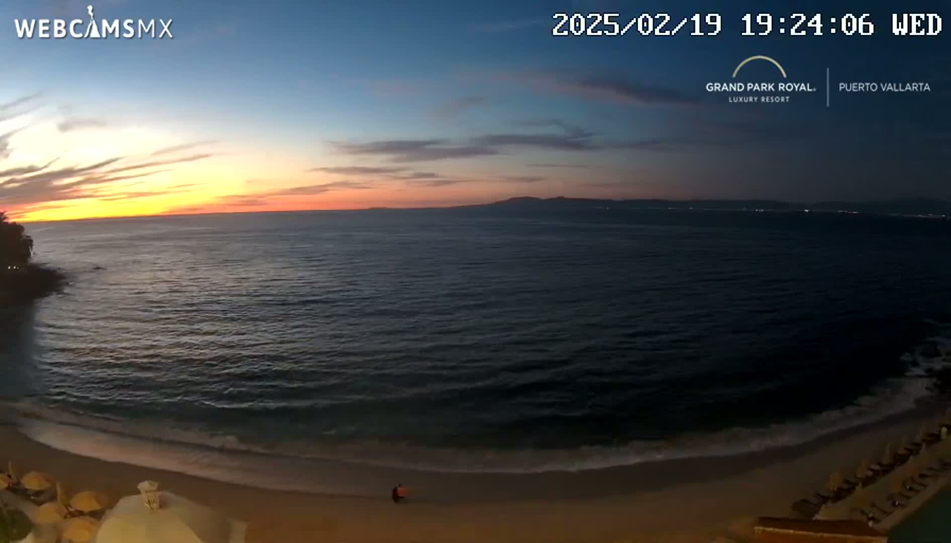A beach at sunset shows calm ocean waves lapping a sandy shore, with a couple walking along the beach and resort amenities visible.