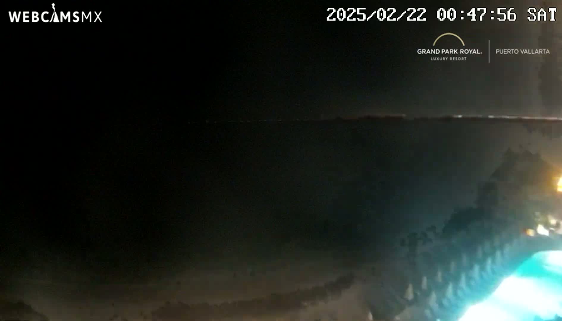 A dark nighttime scene shows a body of water with faint lights on the horizon.