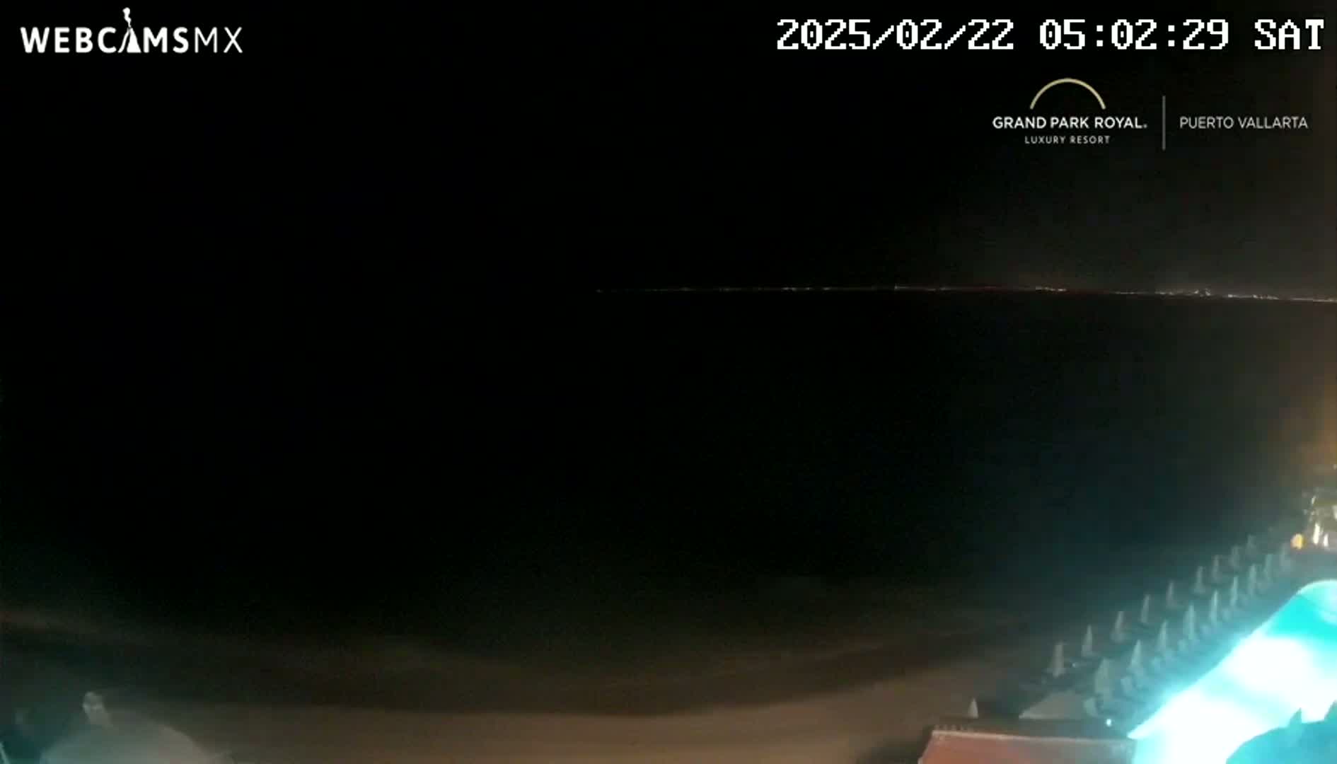 A nighttime, dark beach scene is visible with a faint horizon line and a portion of what appears to be beach furniture illuminated in the bottom right corner.