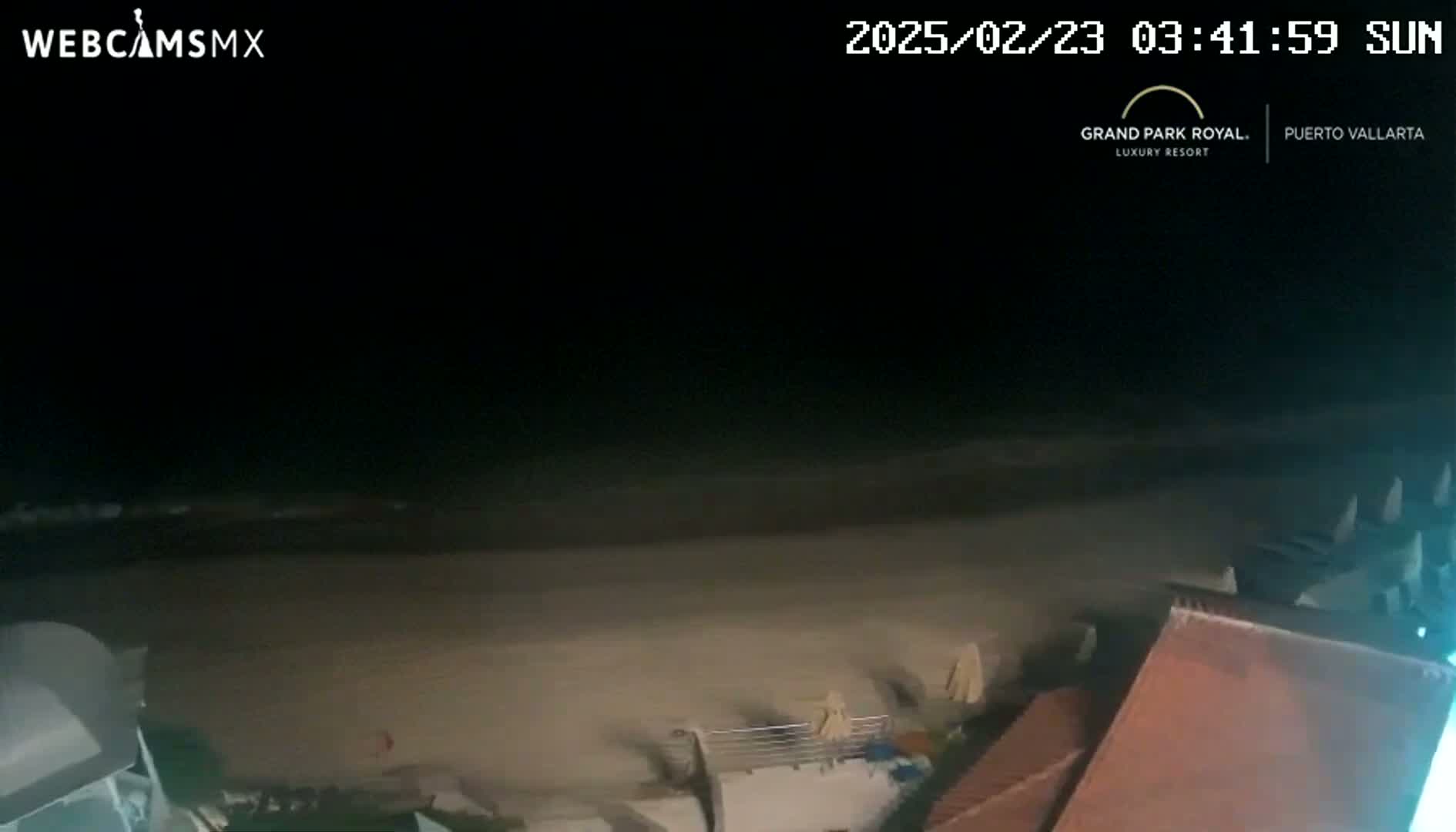 A nighttime view of a mostly empty beach with dark ocean waves under a clear sky.